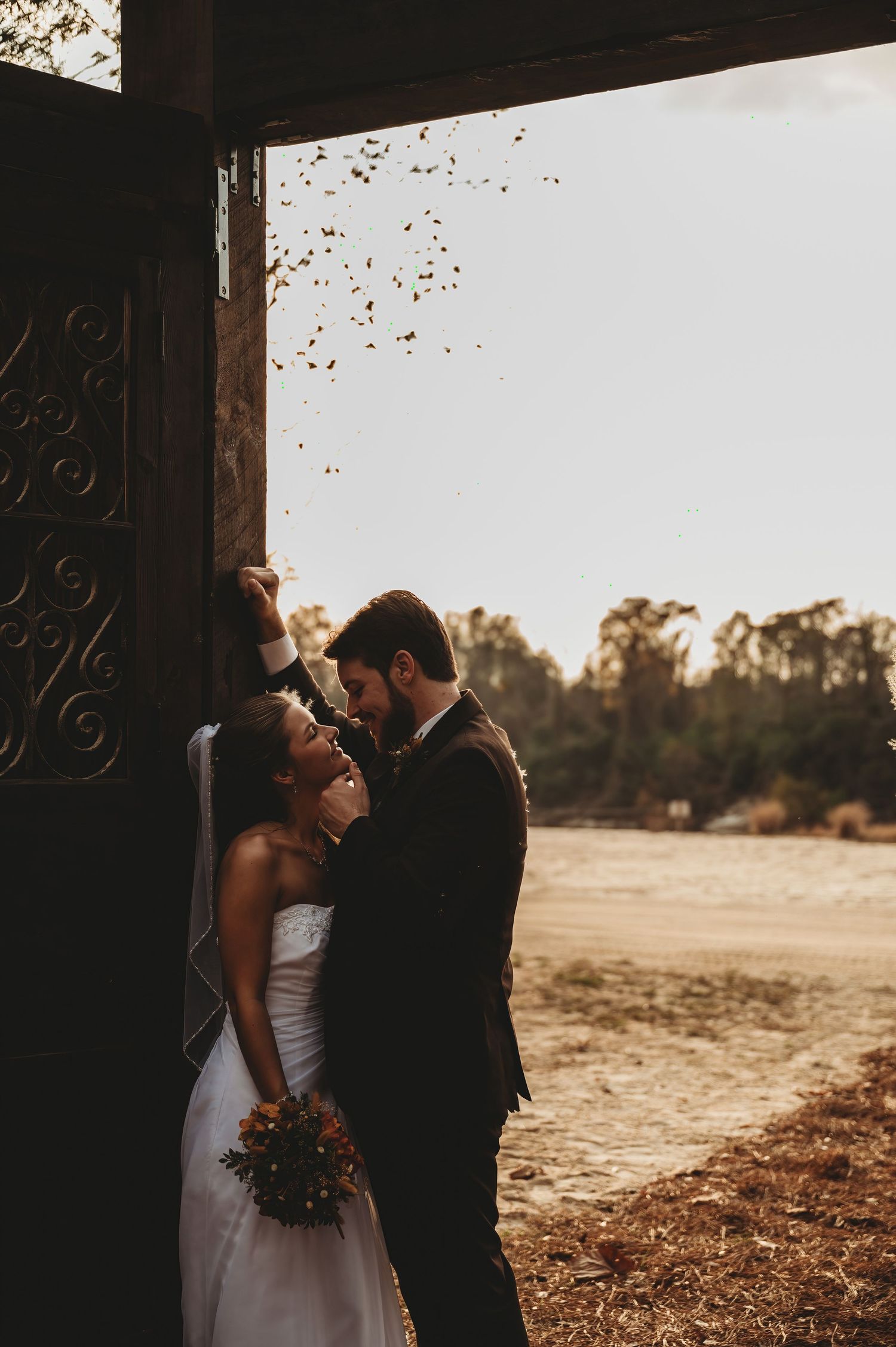 Bride and groom share a romantic moment in a barn doorway, with confetti falling around them on their wedding day.