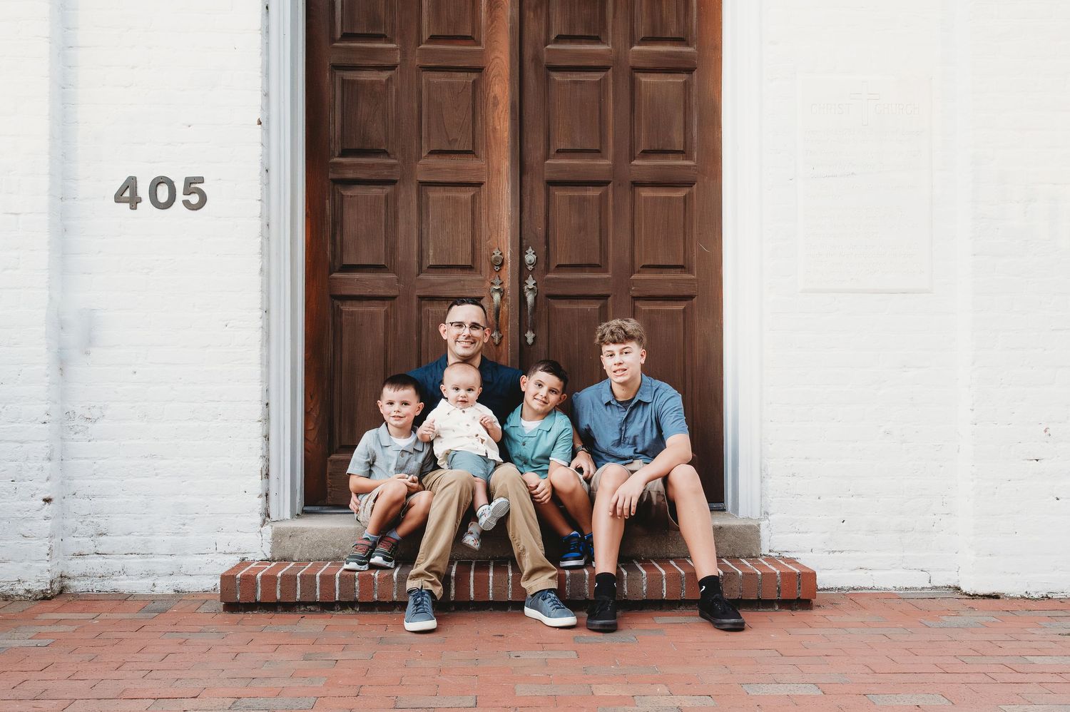 Father sitting with four young sons on brick steps in front of large wooden doors numbered 405.