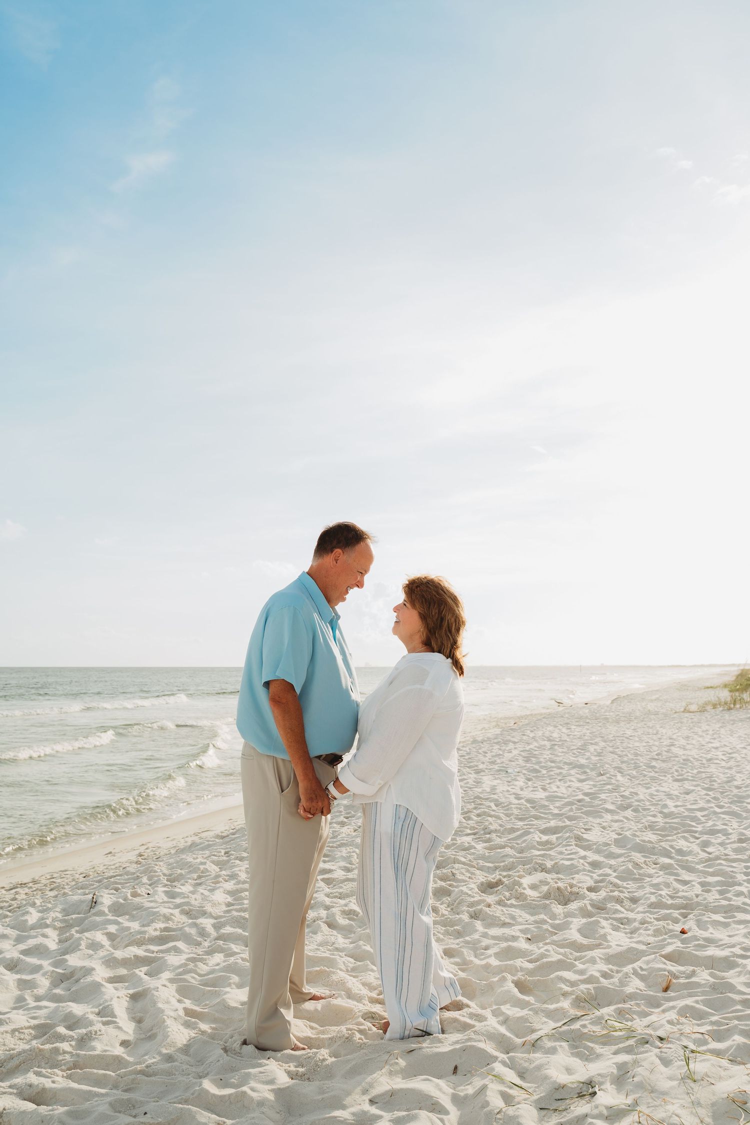 Mature couple holding hands and gazing at each other on a sunny white sand beach.