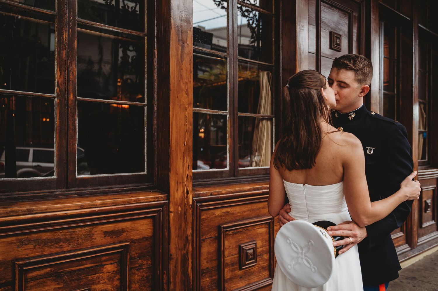 Bride and groom sharing a romantic kiss outside elegant dark wood building in urban wedding setting.
