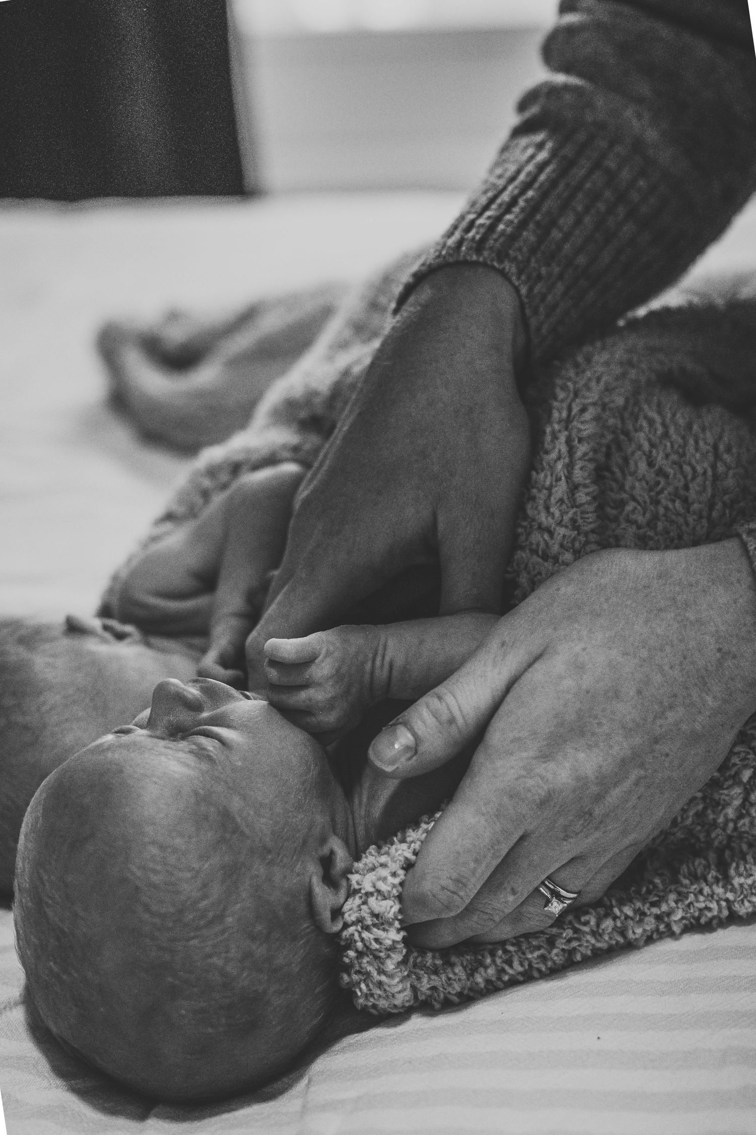 Black and white close-up of parent's hands gently cradling a peaceful newborn baby on a bed.