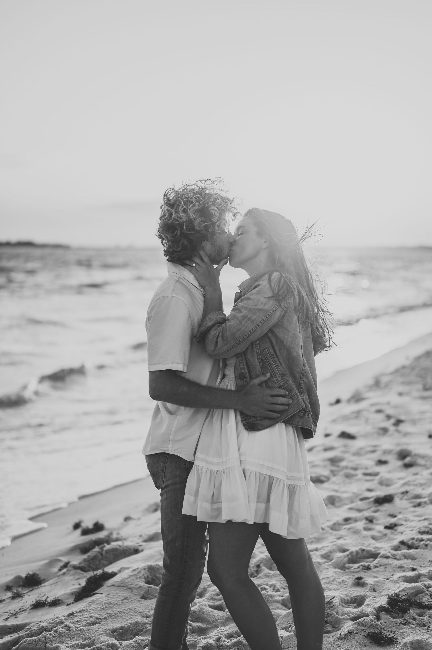 Black and white romantic beach kiss, couple embracing by ocean waves at dusk.