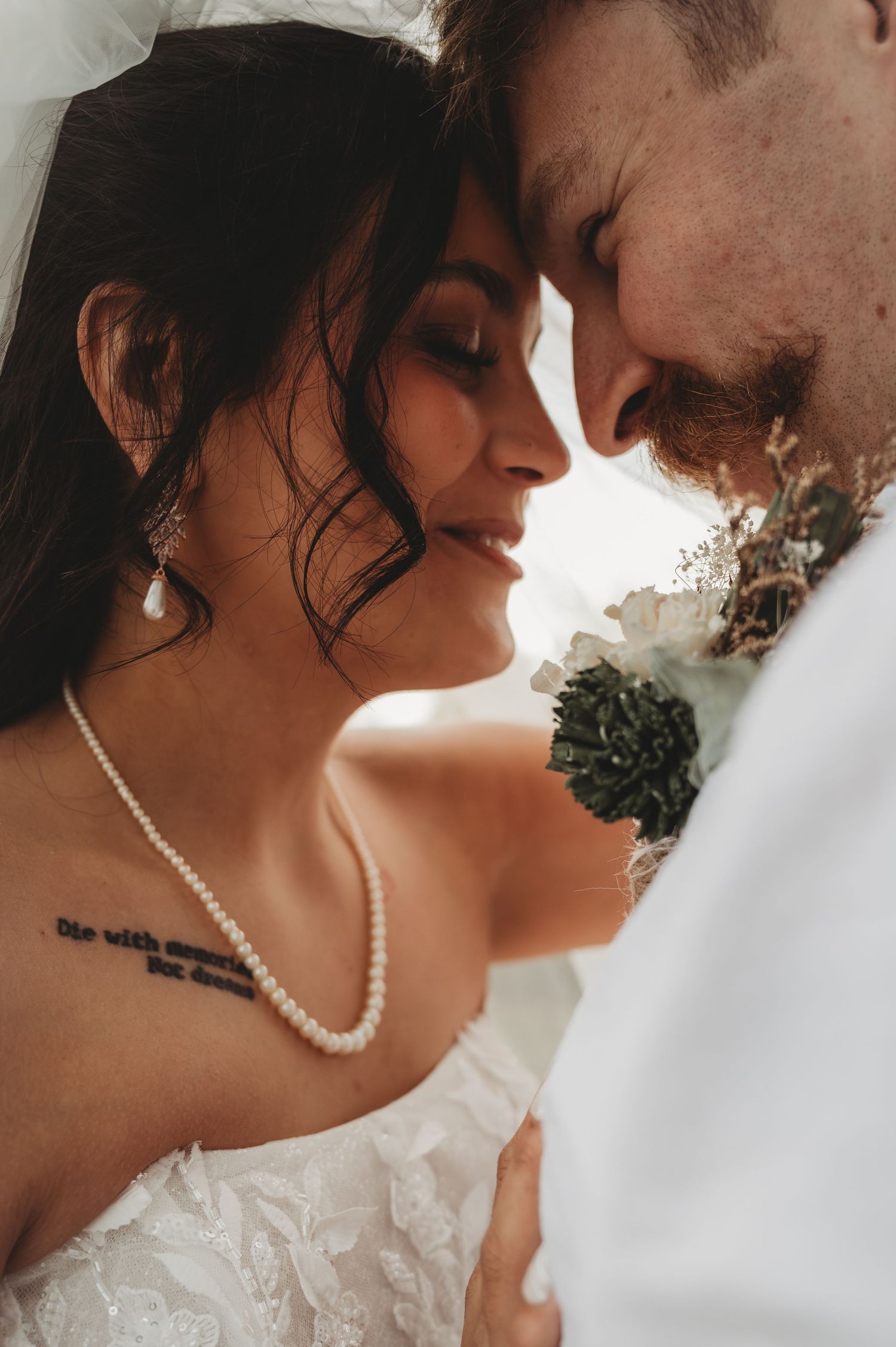 A bride and groom share an intimate forehead touch moment, bride wearing pearl necklace and lace dress on their wedding day.