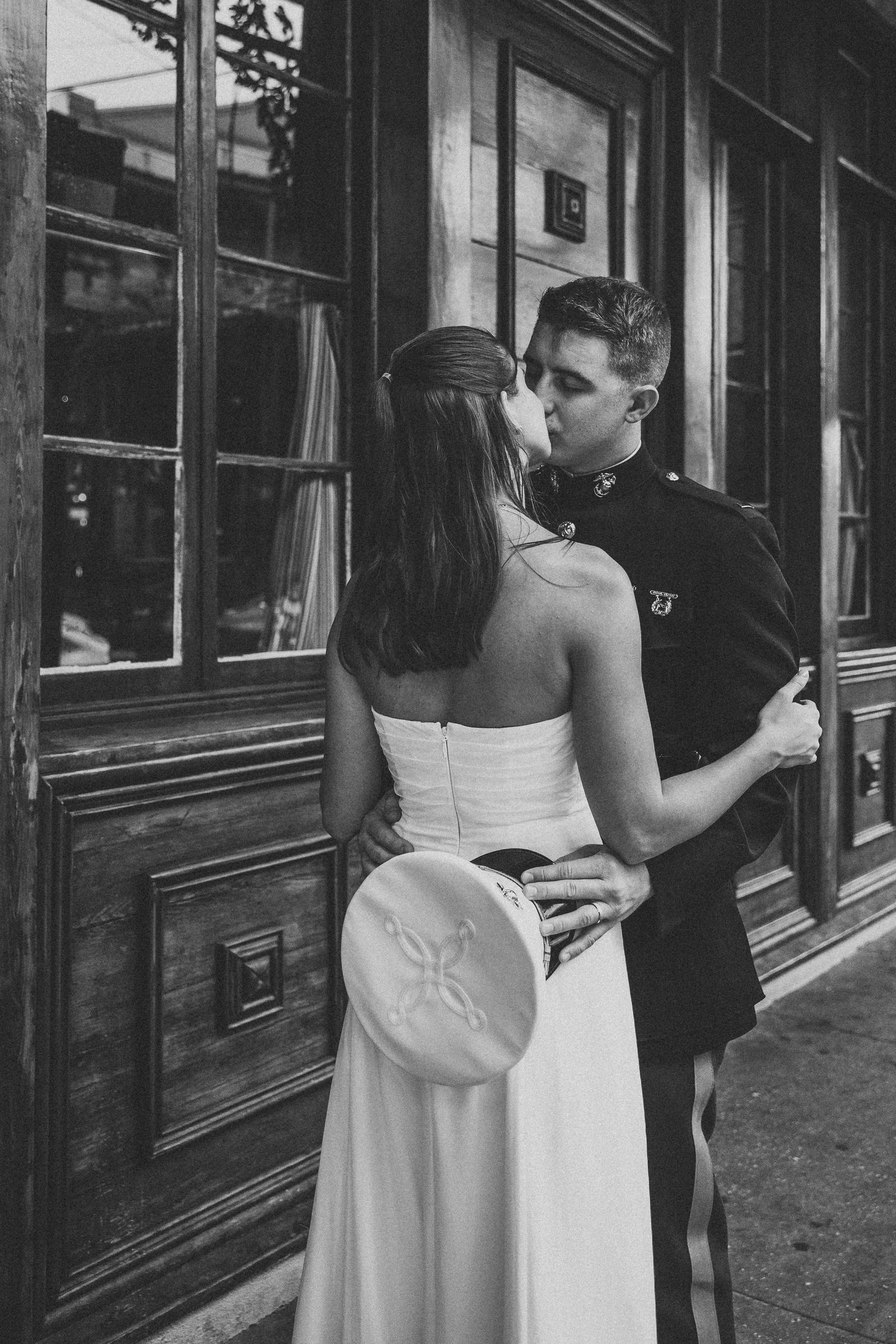 Black and white photo of a bride and groom in military uniform sharing a kiss outside a historic building.