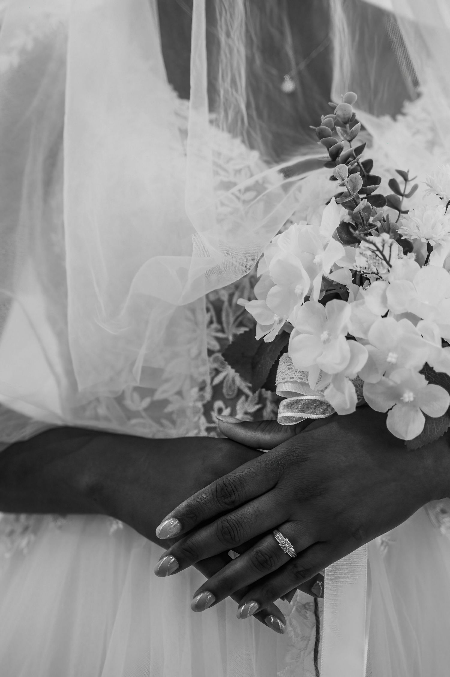 Black and white close-up of bride holding white floral bouquet with diamond wedding ring visible.