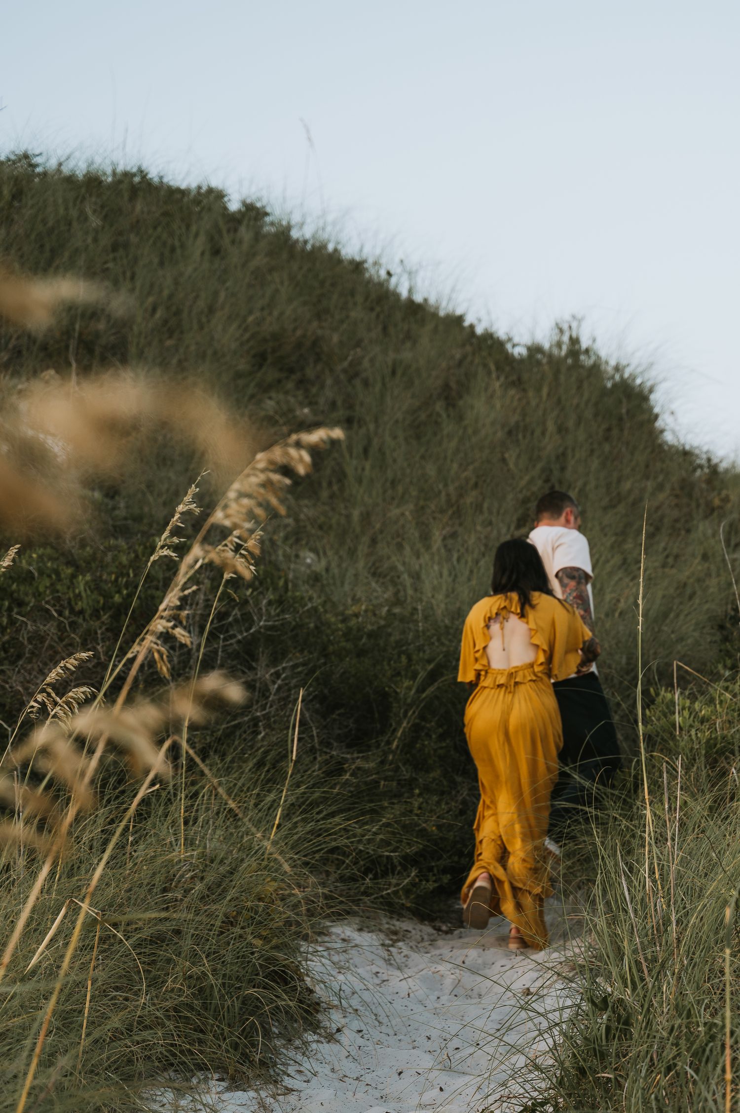 Couple walking up a sandy path through tall beach grass and sand dunes.