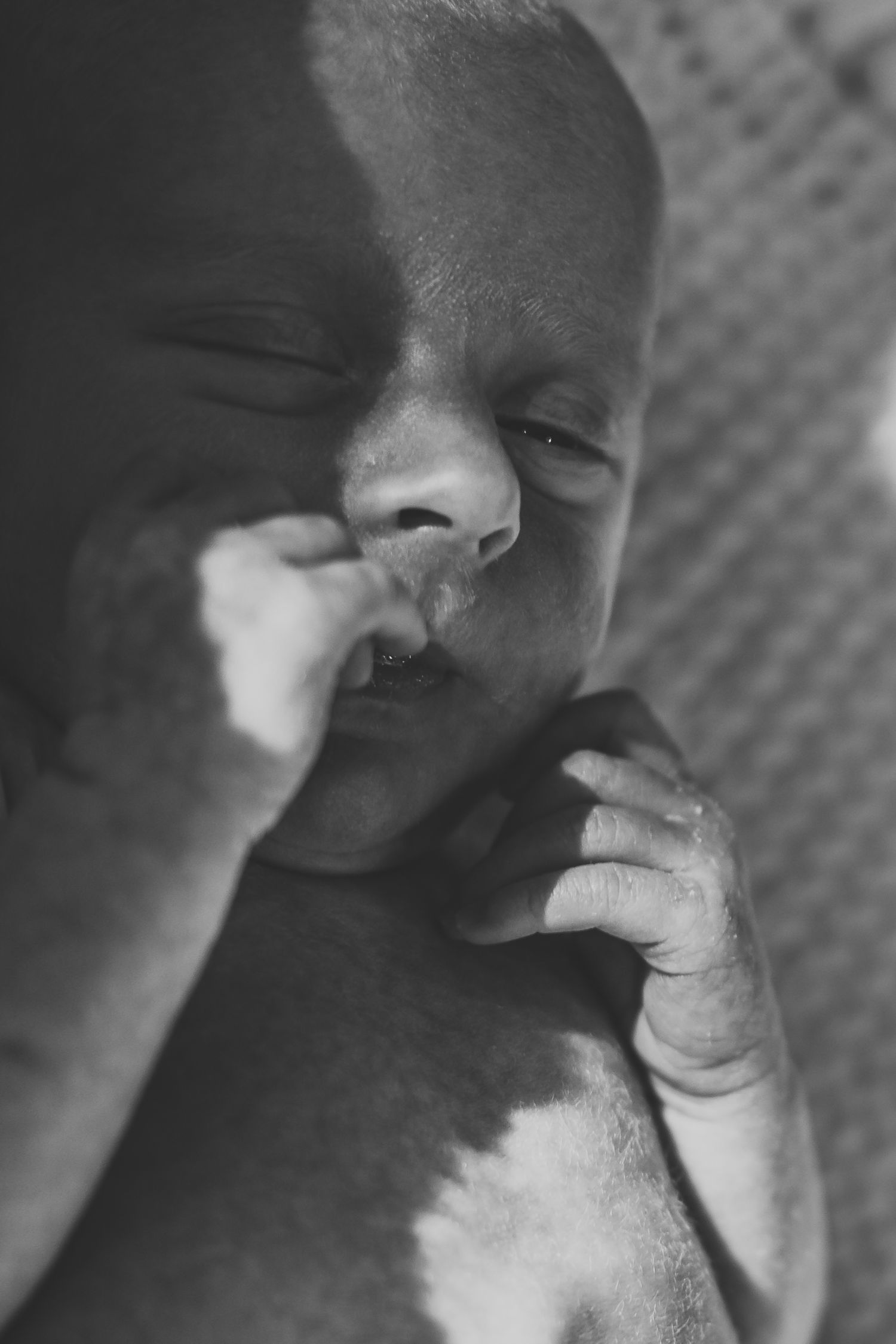 Black and white close-up portrait of a sleeping newborn baby with tiny hand near face.