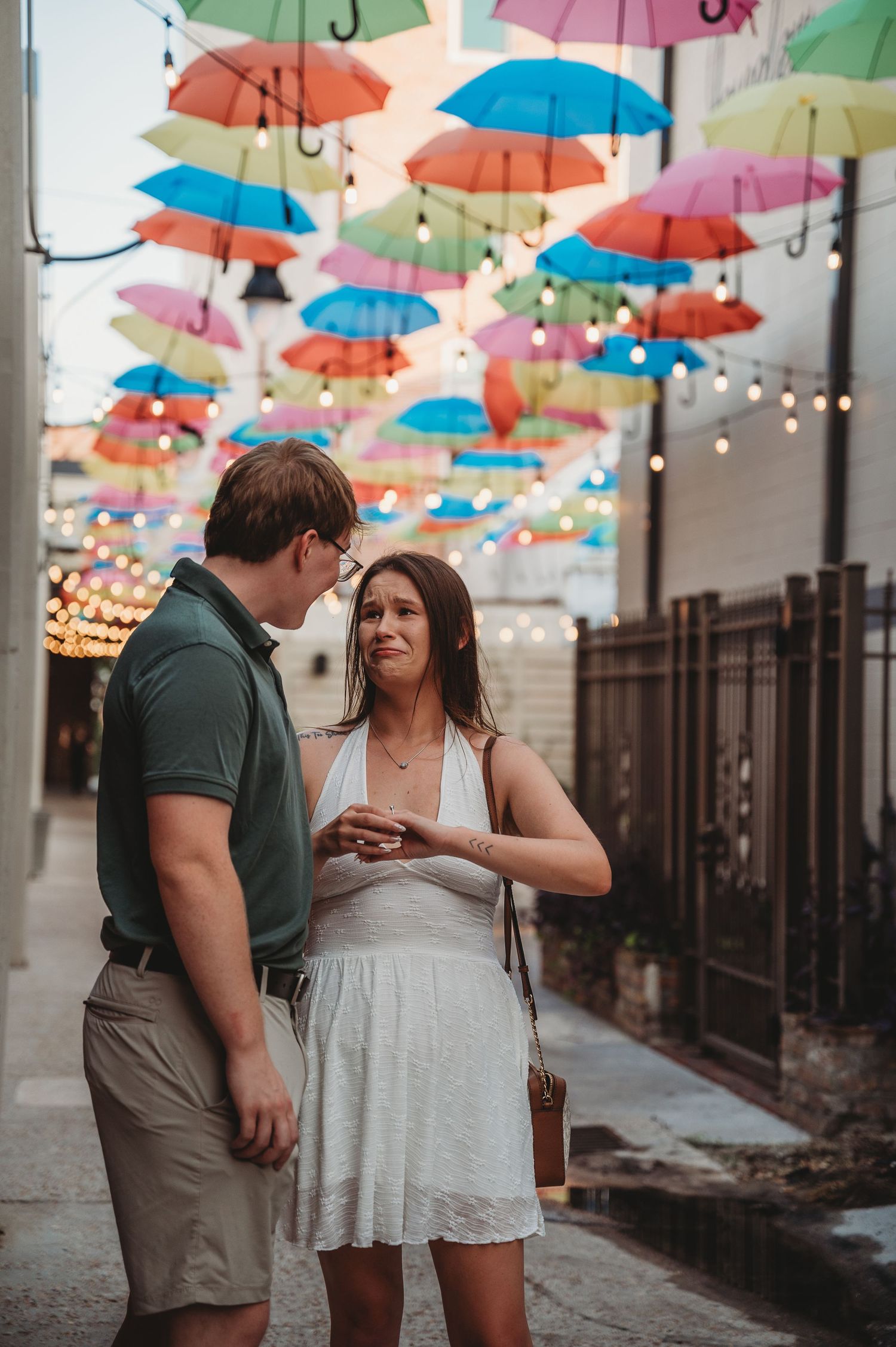 Couple sharing a romantic moment under colorful hanging umbrellas in a festive outdoor alley.