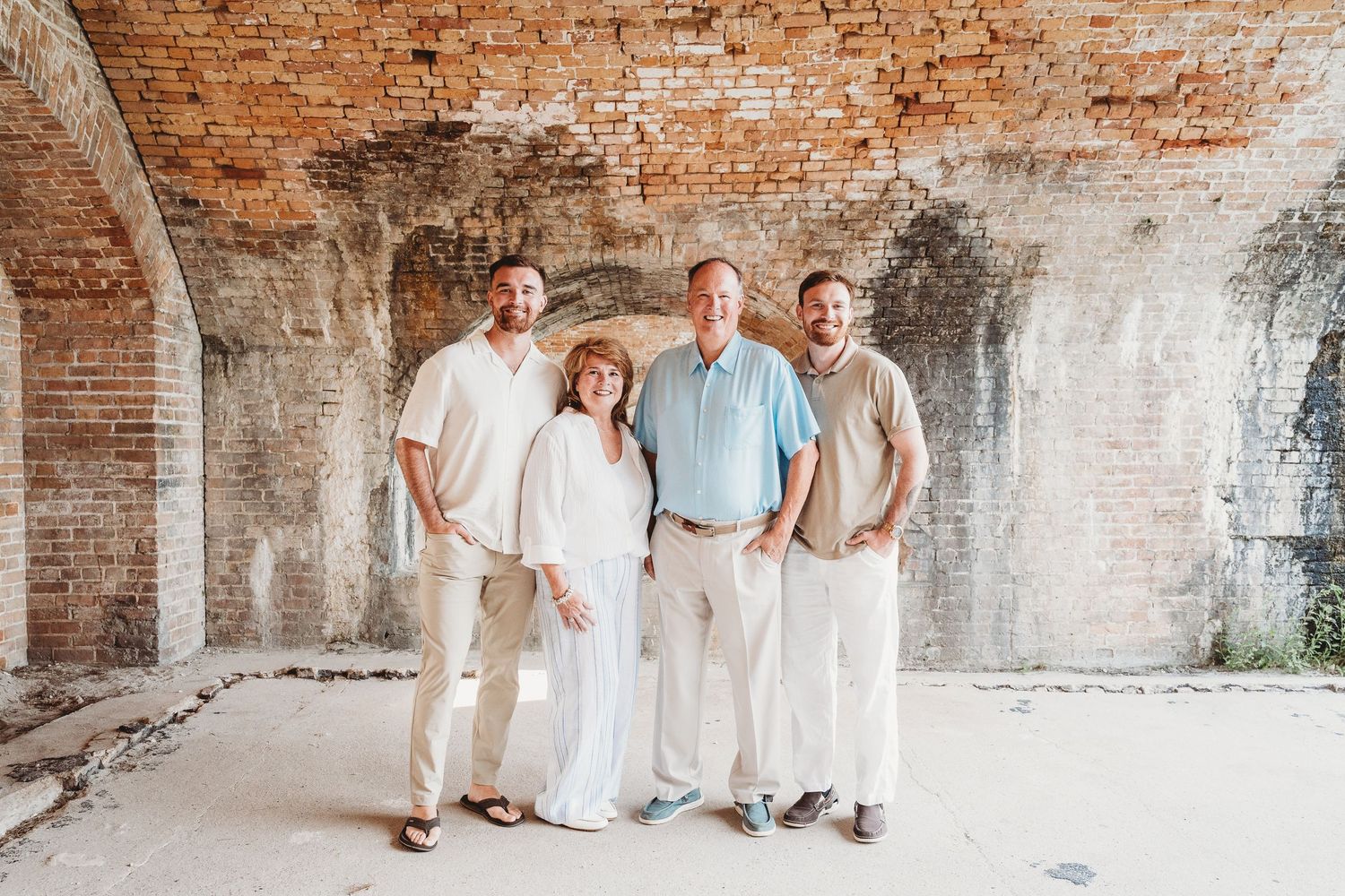 Family of four smiling together inside a rustic brick archway at a historic landmark.