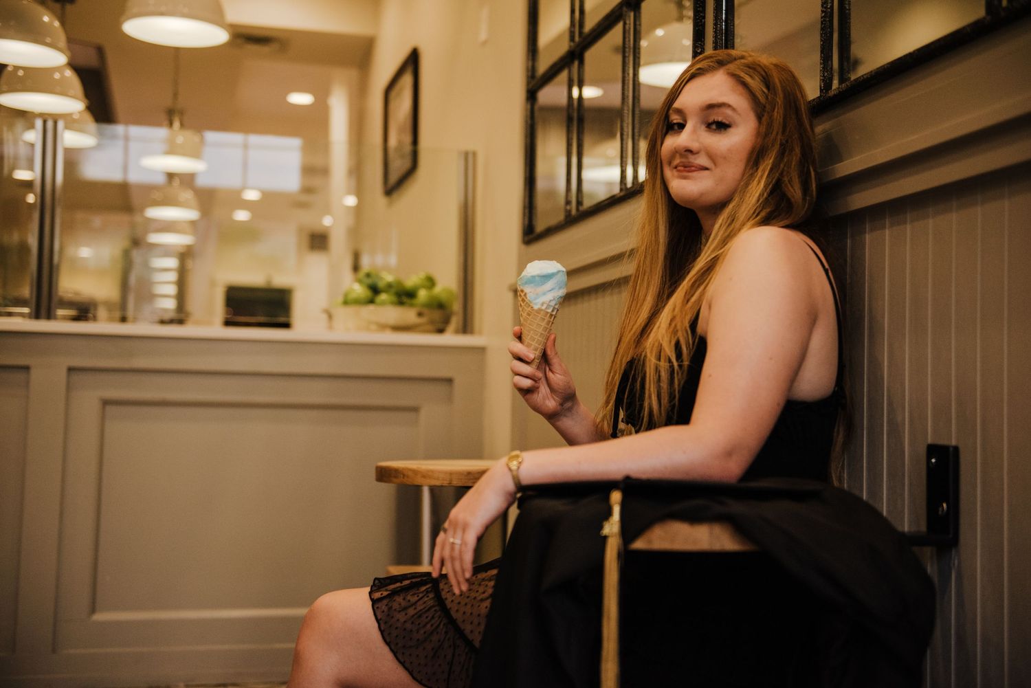 A young woman with long red hair holds an ice cream cone while seated in a cafe.