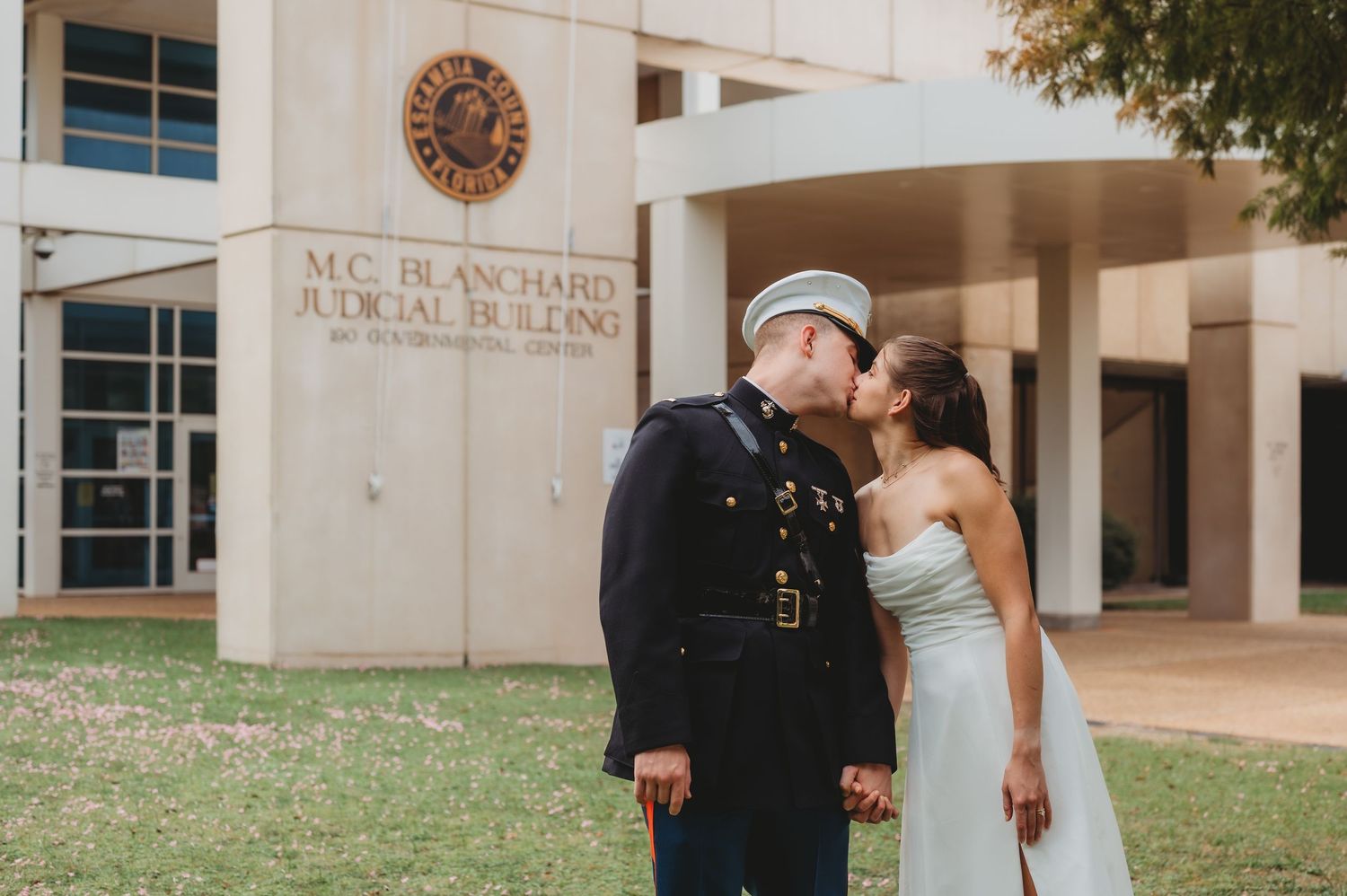 Marine in dress uniform kisses bride in white strapless gown outside M.C. Blanchard Judicial Building.