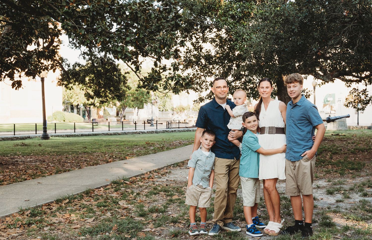 A happy family of five poses together under a large tree in a scenic park.