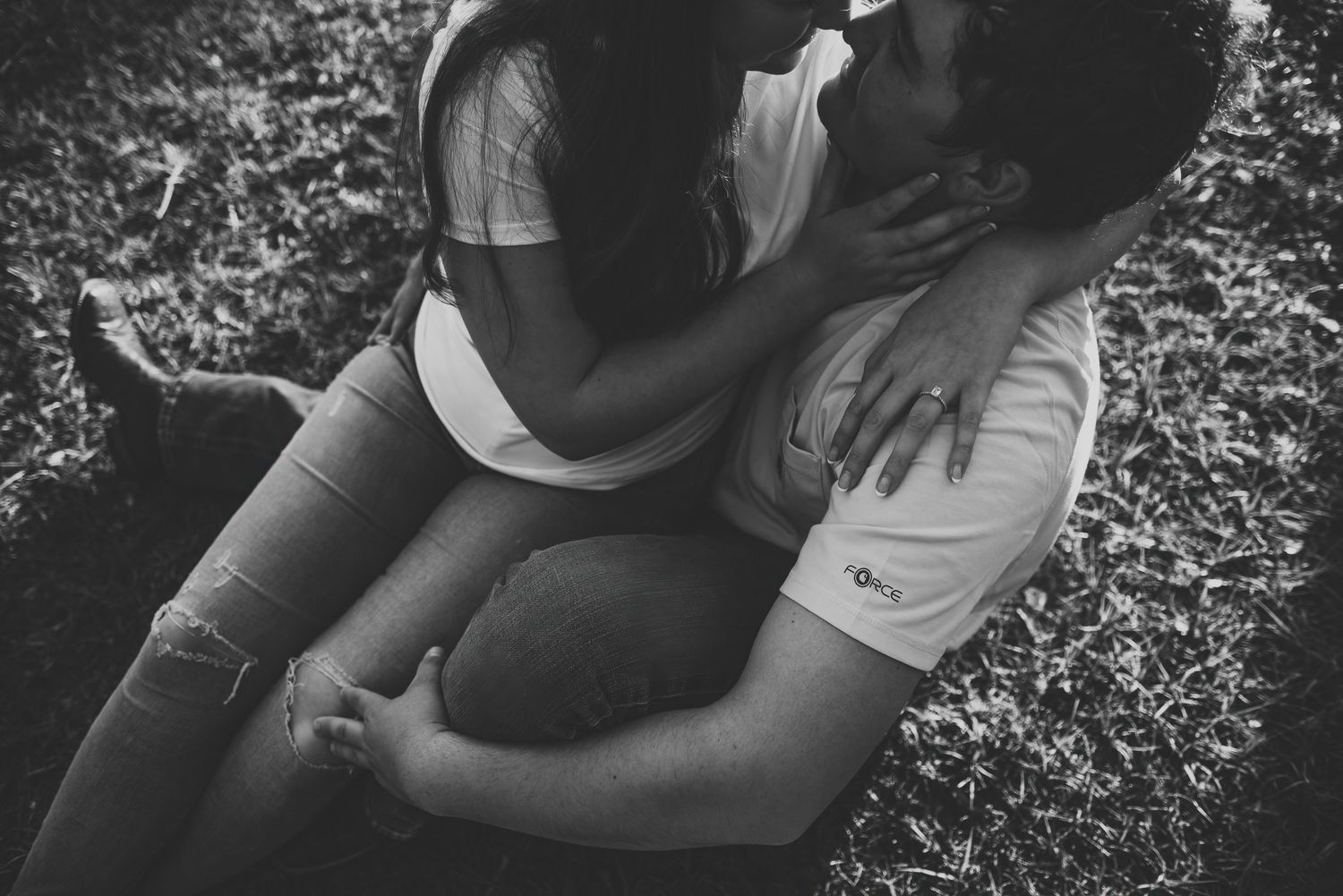 Black and white photo of a couple sharing a romantic kiss while lying on grass outdoors.