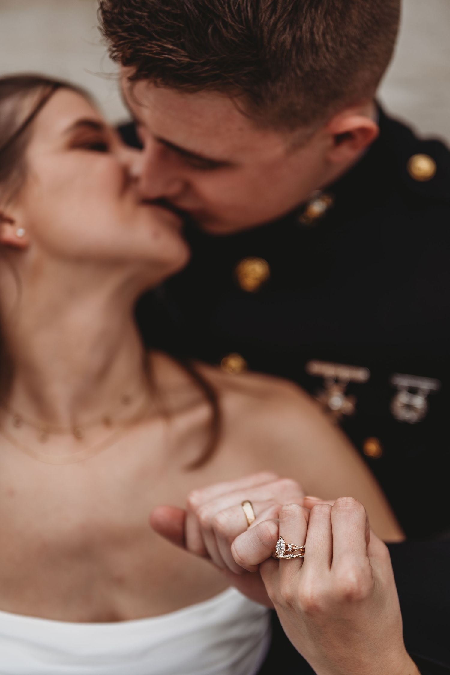 Couple shares a kiss while displaying bride's diamond engagement ring and gold wedding band.
