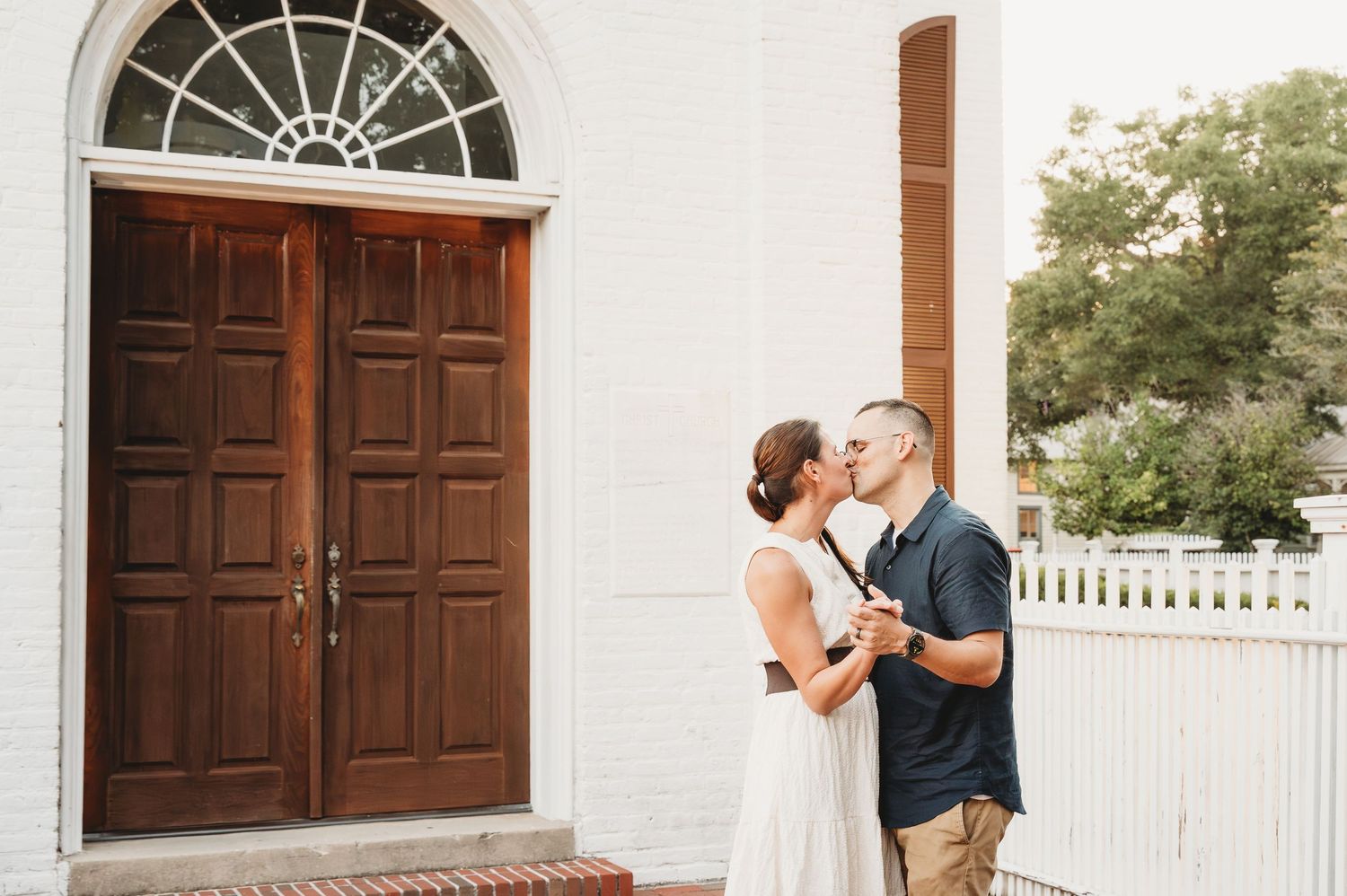 Couple sharing a kiss outside a white historic building with large wooden double doors.