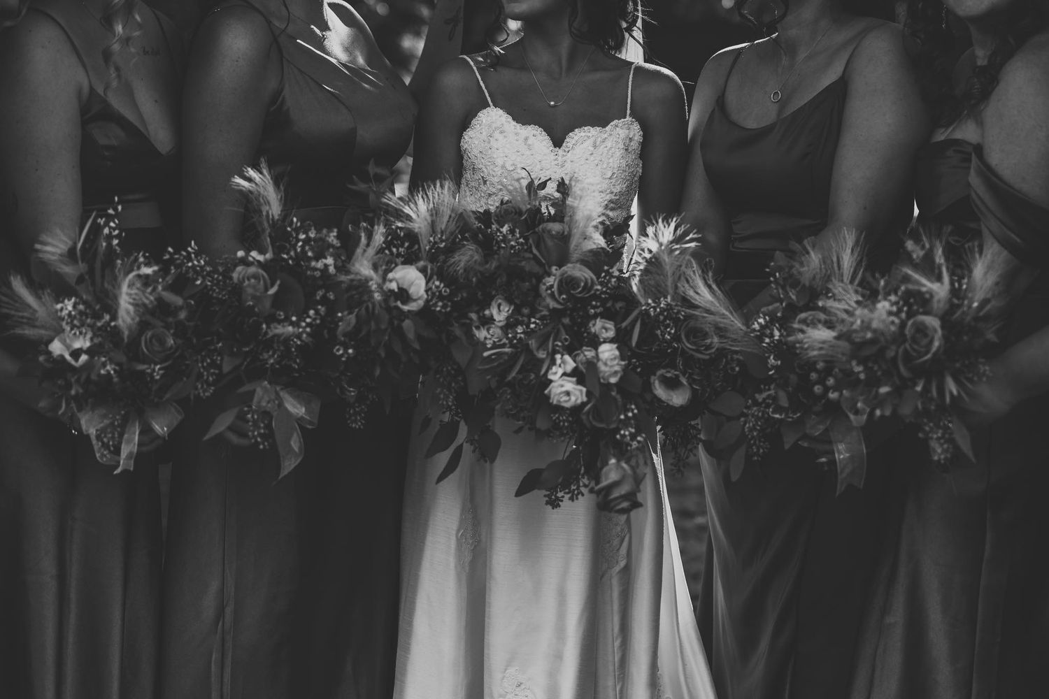 Black and white photo of bride and bridesmaids in dark gowns holding lush floral bouquets.
