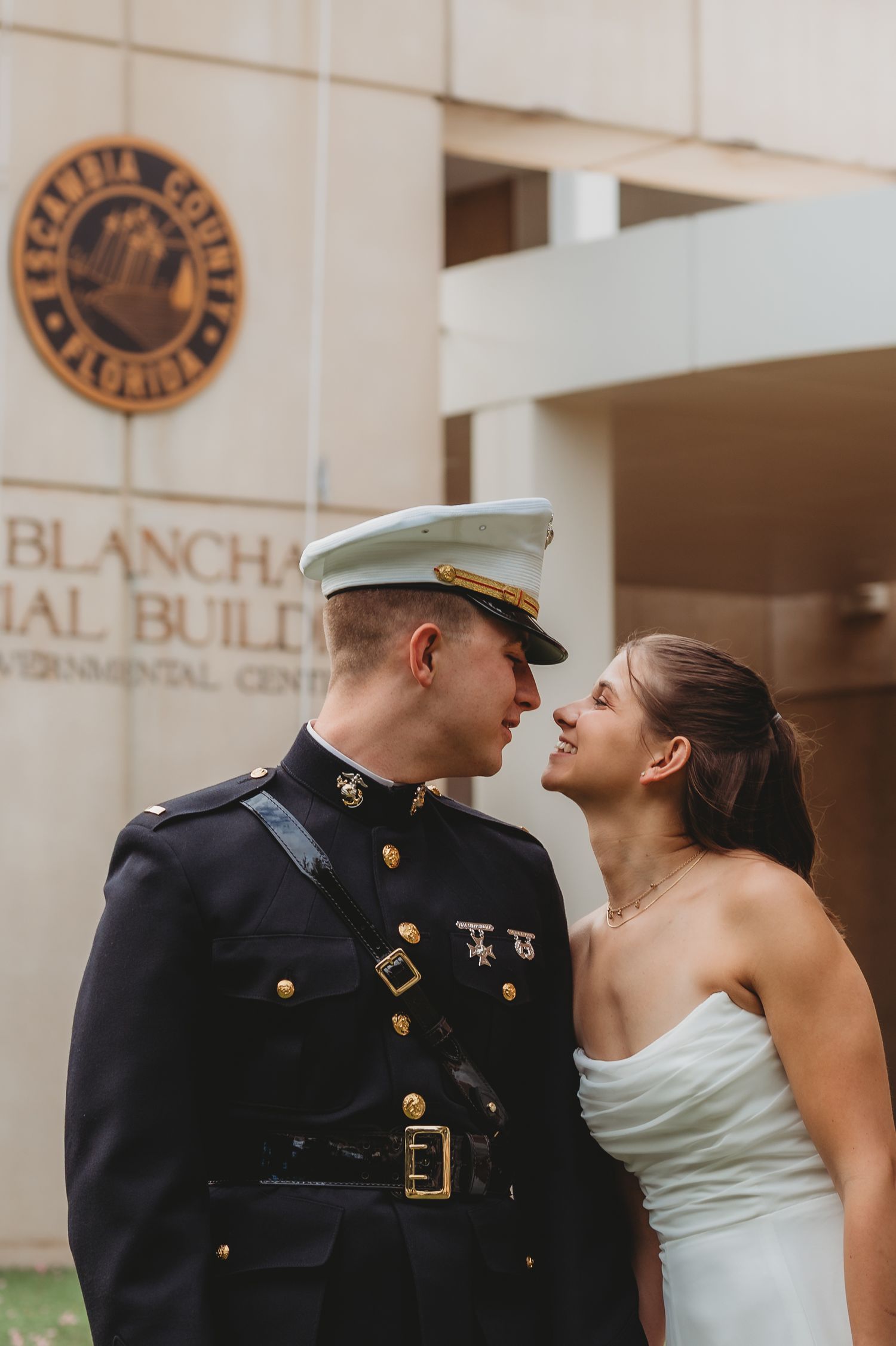 Marine in dress uniform and bride in white gown share a romantic moment outside Escambia County Blanchard Building.