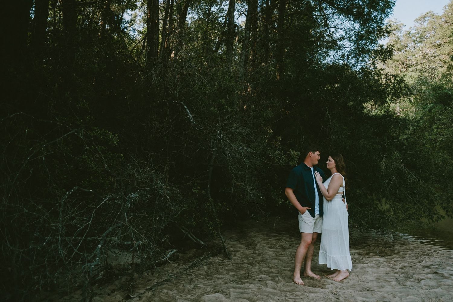 Couple sharing a tender moment on a sandy path surrounded by dense green forest trees.