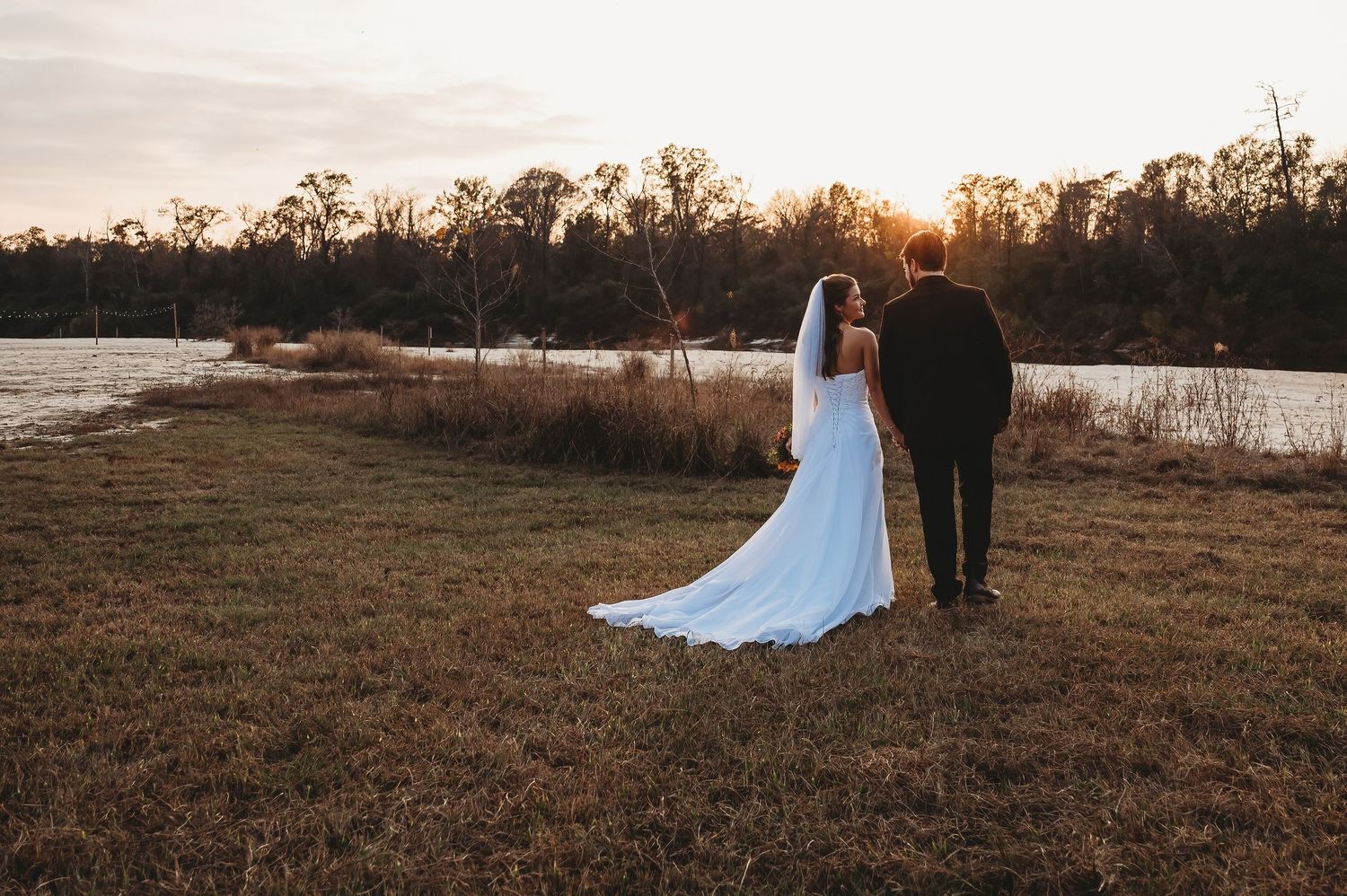 Bride and groom holding hands watching a golden sunset over a serene lake at their wedding.