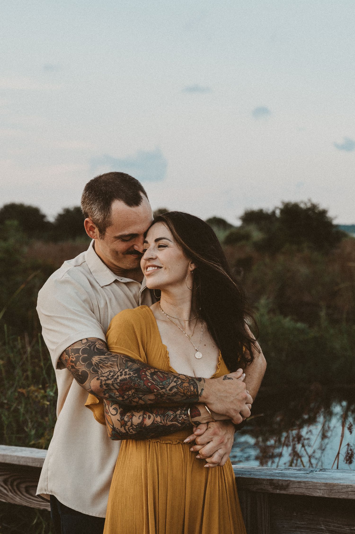 Man embracing smiling woman in mustard yellow dress at sunset.