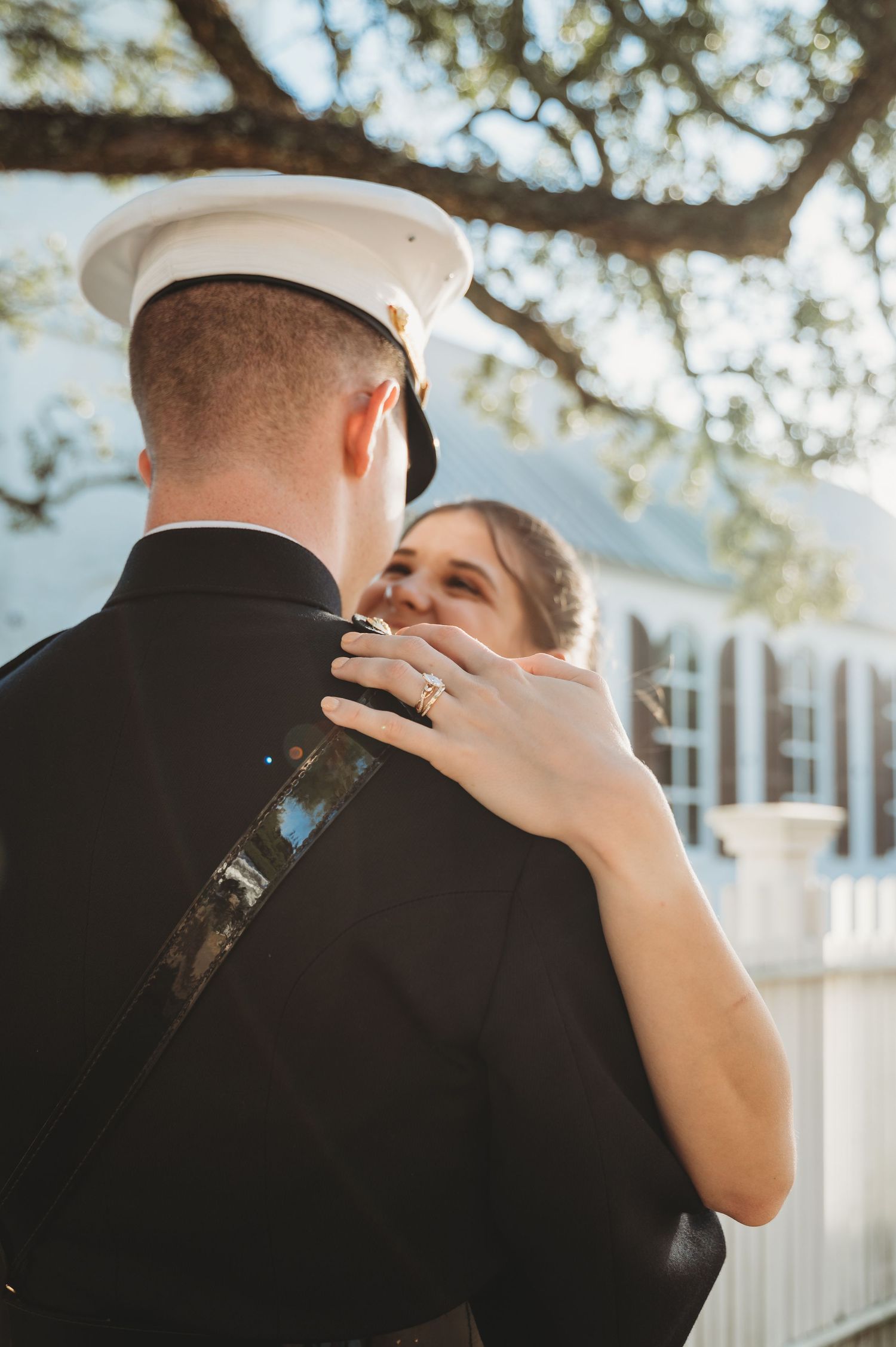 Smiling bride places hand on Marine groom's shoulder during outdoor first dance in golden light.