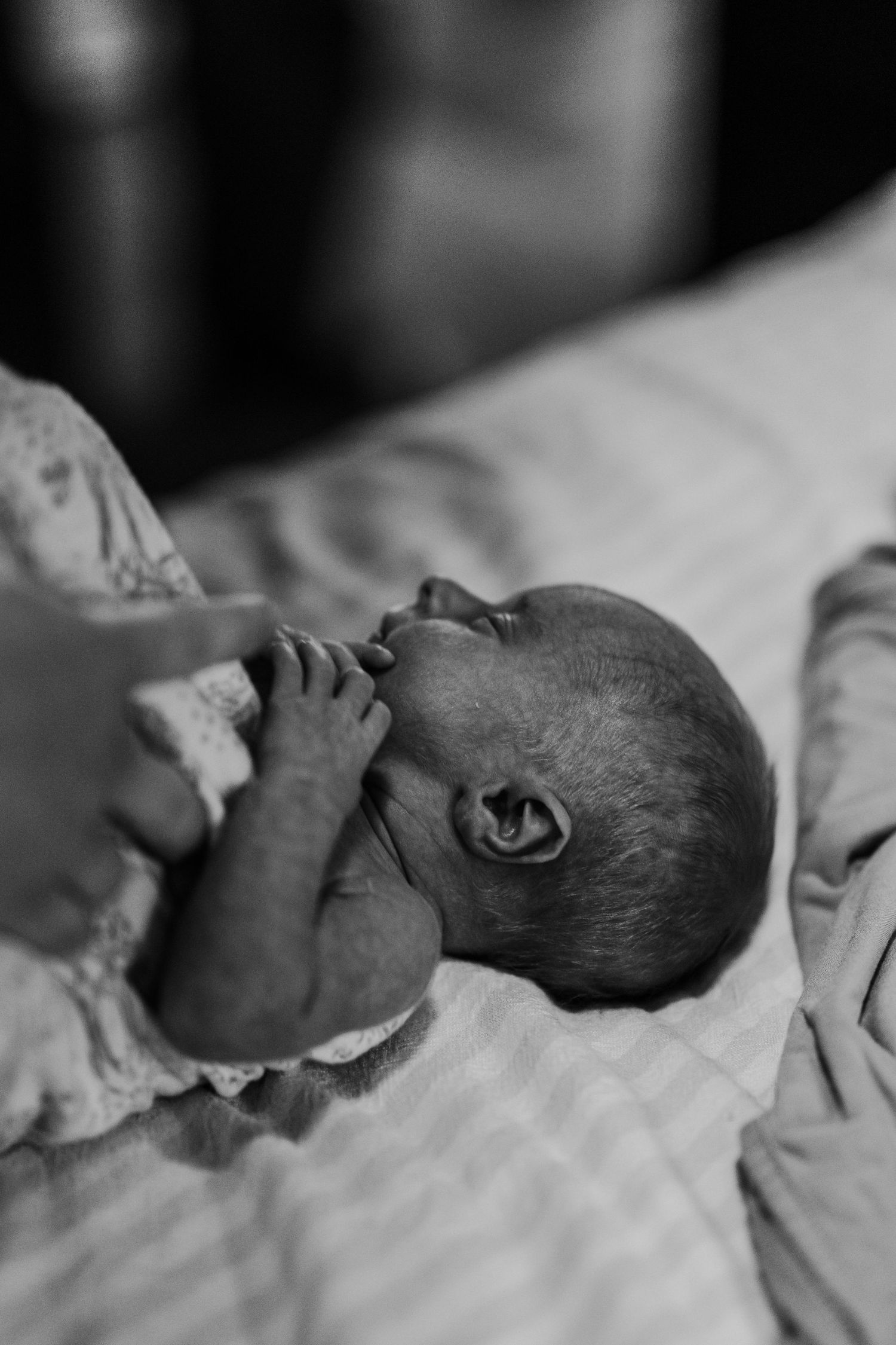 Black and white close-up of a newborn baby breastfeeding while gently holding mothers finger.