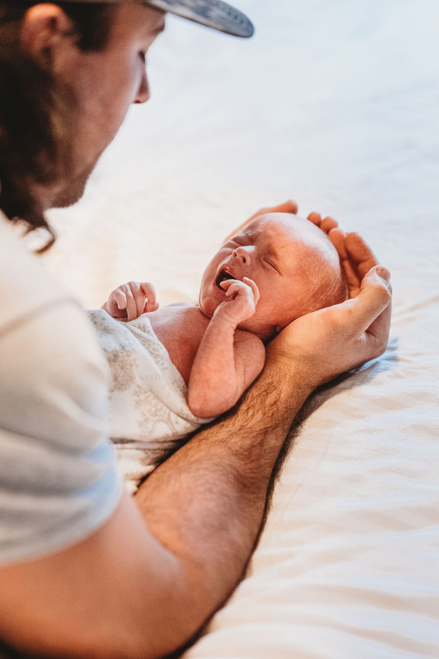 Father tenderly cradling smiling newborn baby on white bed, gentle bonding moment.