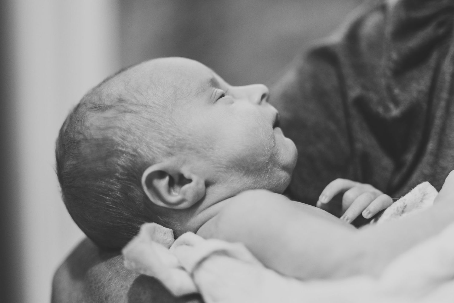Black and white close-up of newborn baby lying back in caring adult hands.