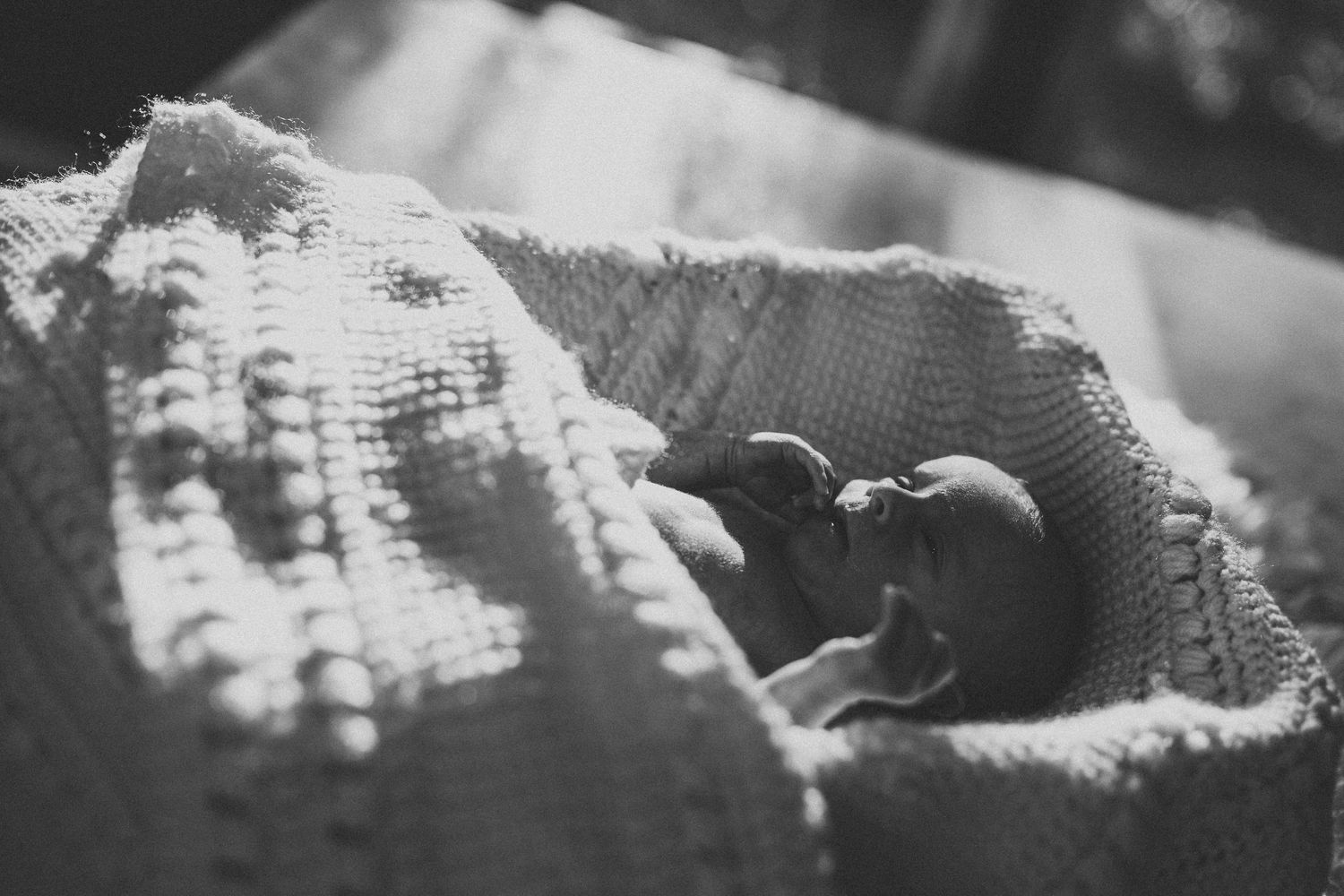 Black and white close-up of a newborn baby peeking out from a textured knit blanket.
