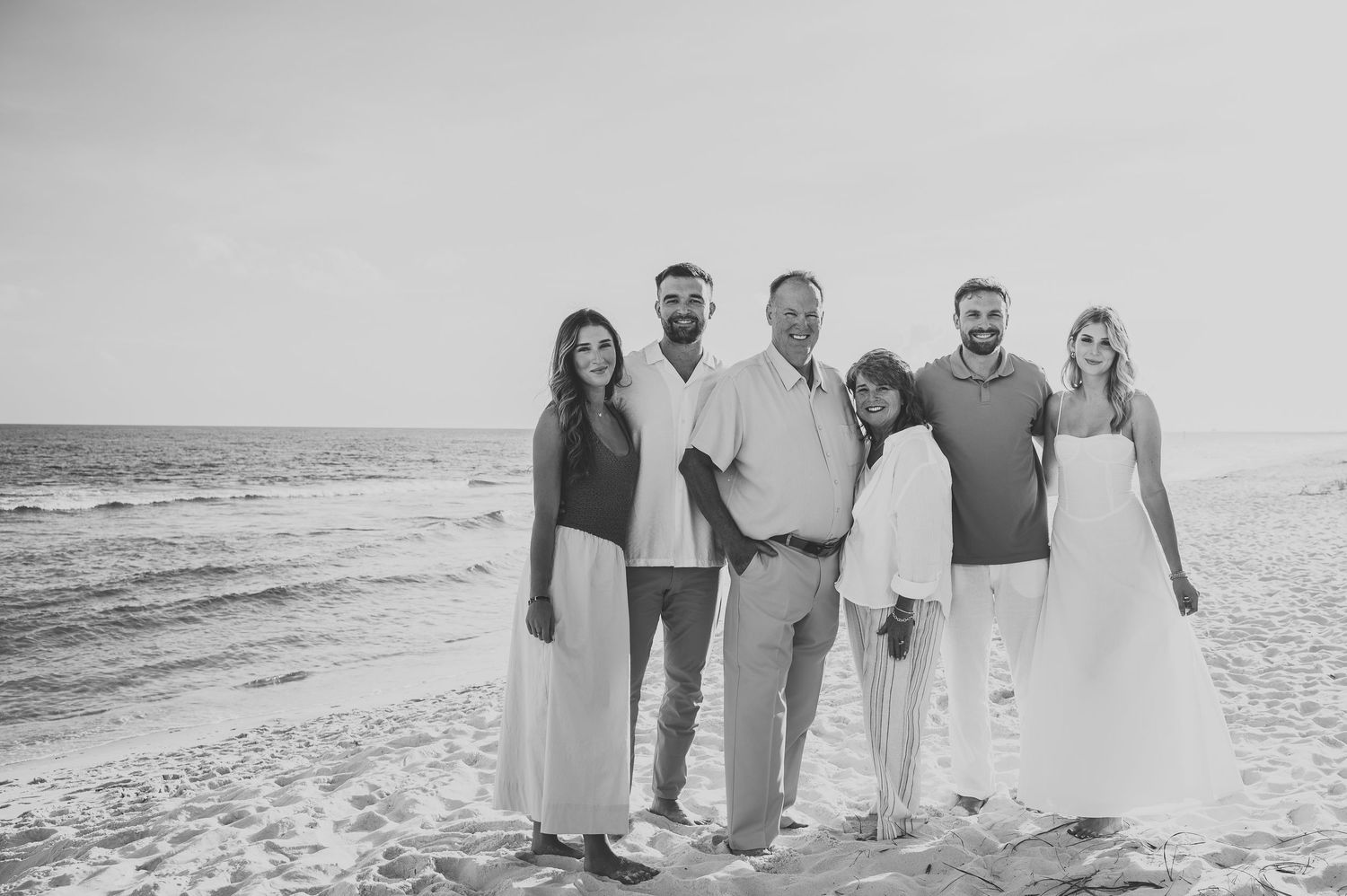 Black and white photo of a family of six posing together on a beach at sunset.