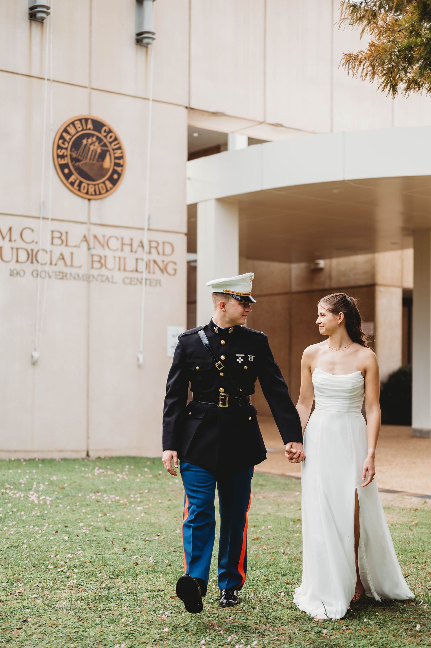 Marine in dress uniform walks hand-in-hand with bride in white gown outside M.C. Blanchard Judicial Building.