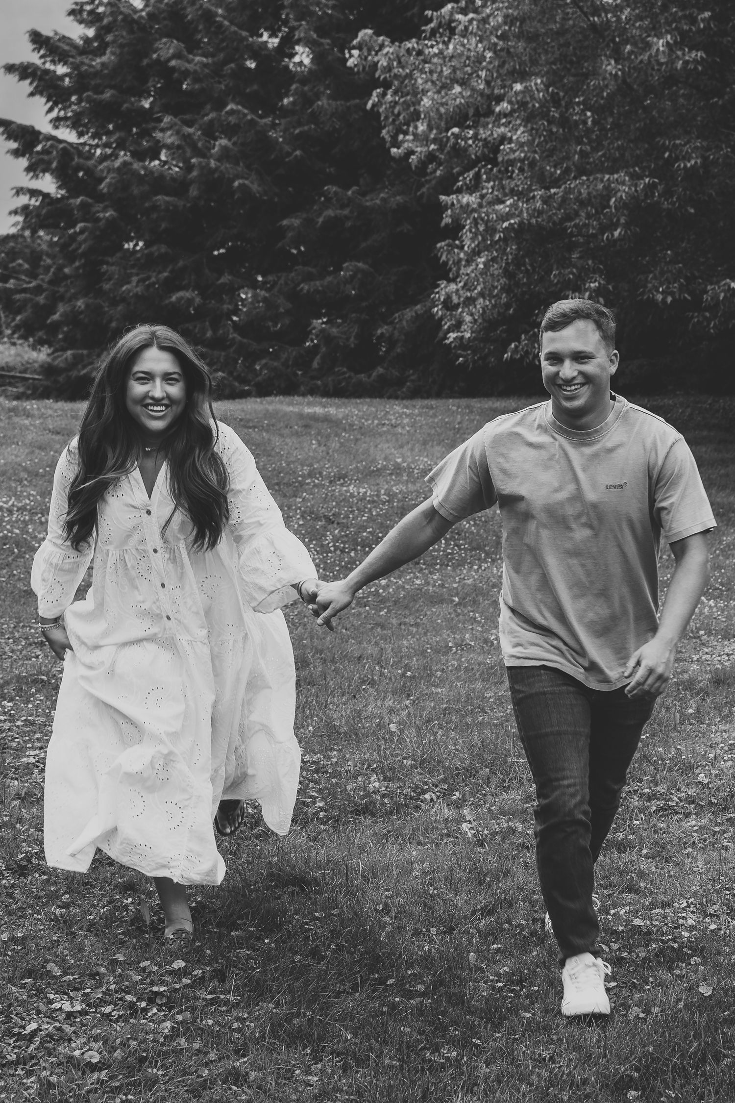 Black and white photo of a happy couple holding hands and walking through a lush green park.