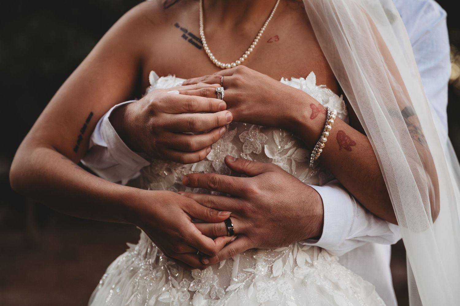 Close-up of bride and groom hands embracing at wedding, showing pearl bracelet, necklace, and wedding ring.