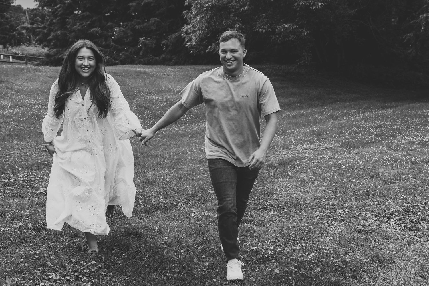 Happy couple holding hands and running through a lush green park in a black and white photo.