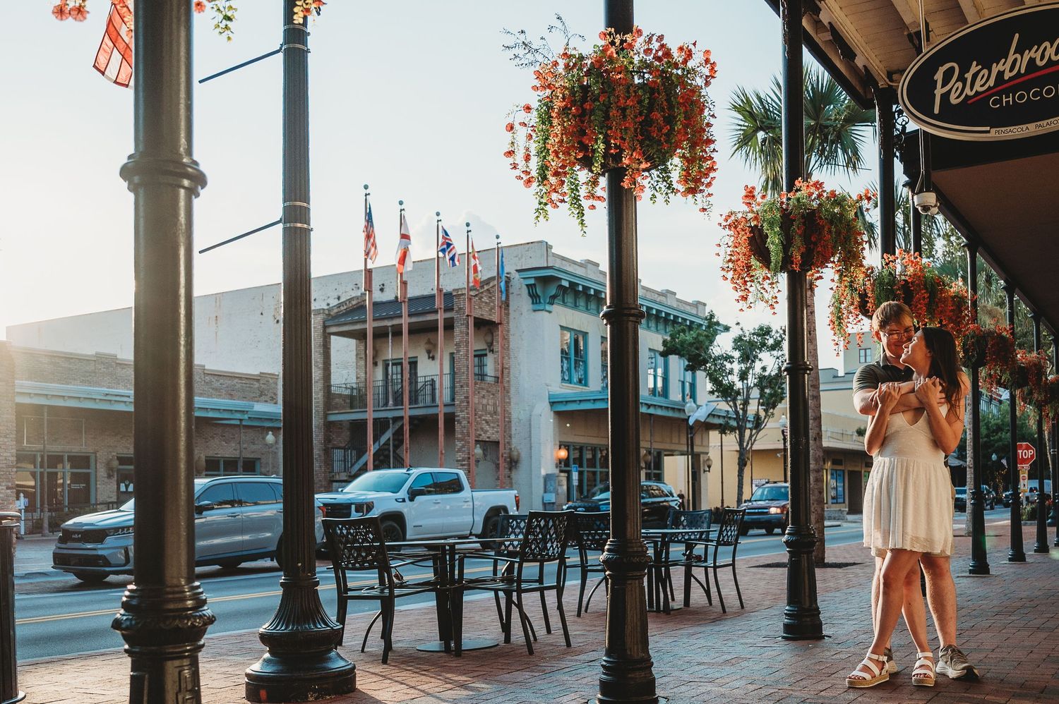 Romantic couple embracing near decorative flower baskets on a sunny downtown street at golden hour.
