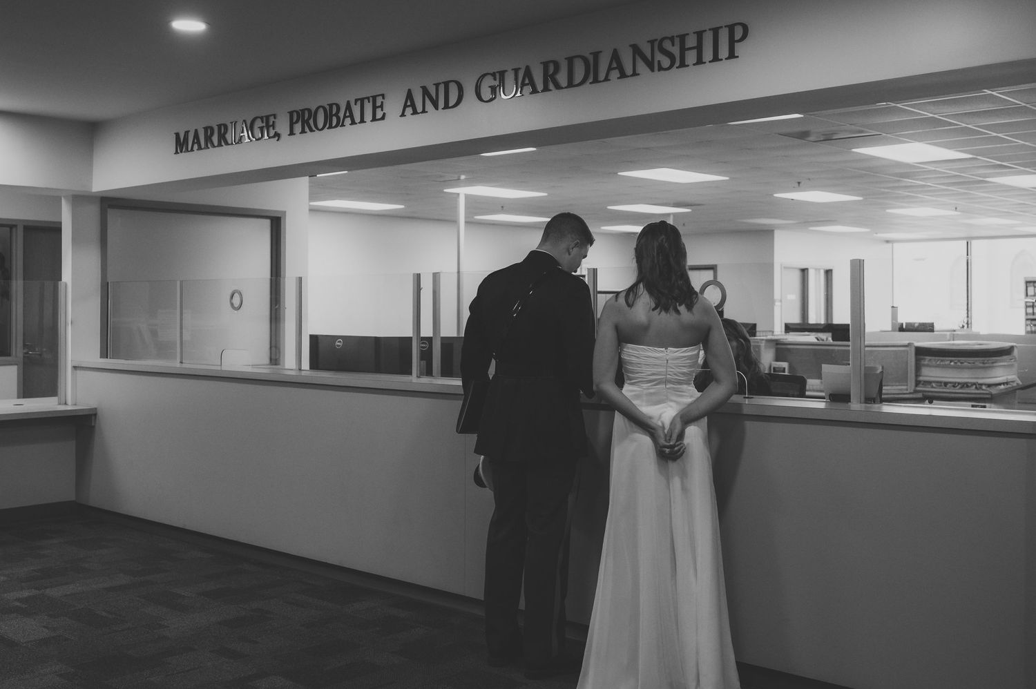 Black and white photo of a couple in wedding attire at a Marriage, Probate and Guardianship office counter.