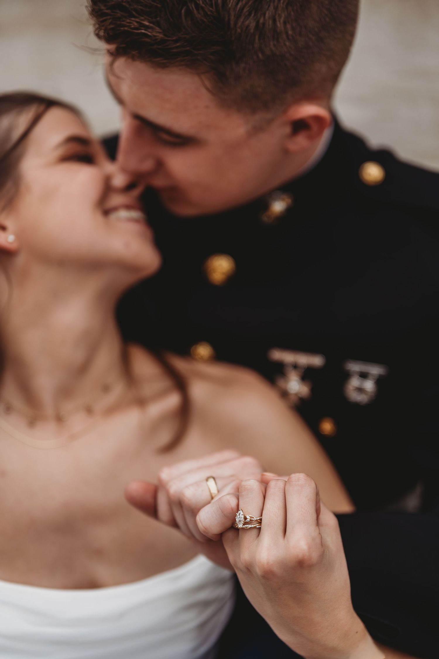 Marine groom in dress blues nearly kissing smiling bride, showcasing wedding rings in romantic close-up photo.