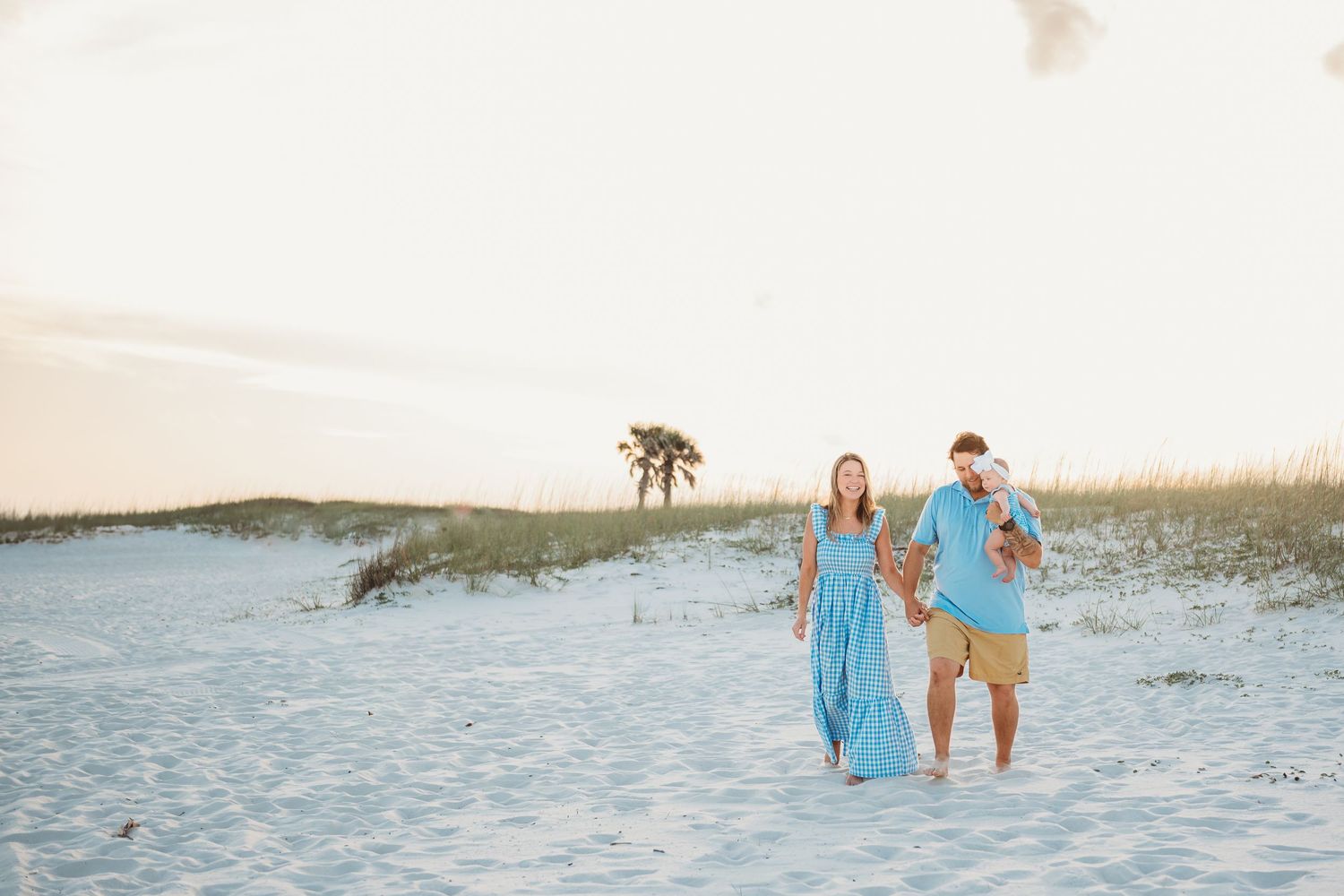 Happy couple in blue outfits strolling on a white sand beach at golden hour.