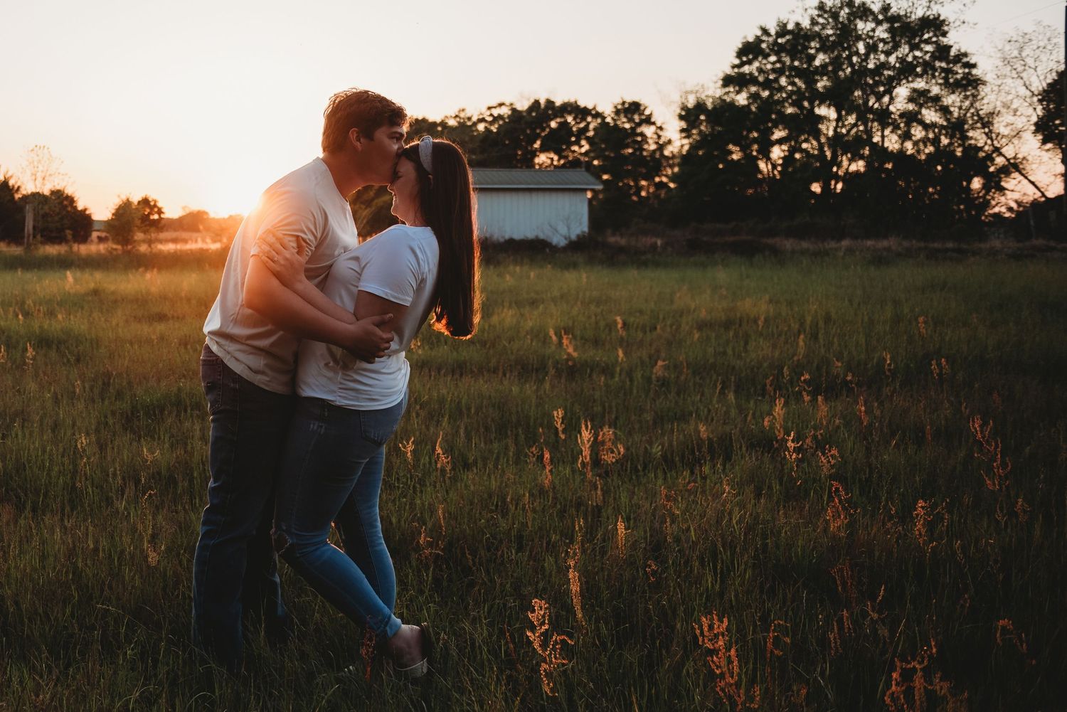 Couple sharing a romantic kiss in a golden meadow during a beautiful sunset.