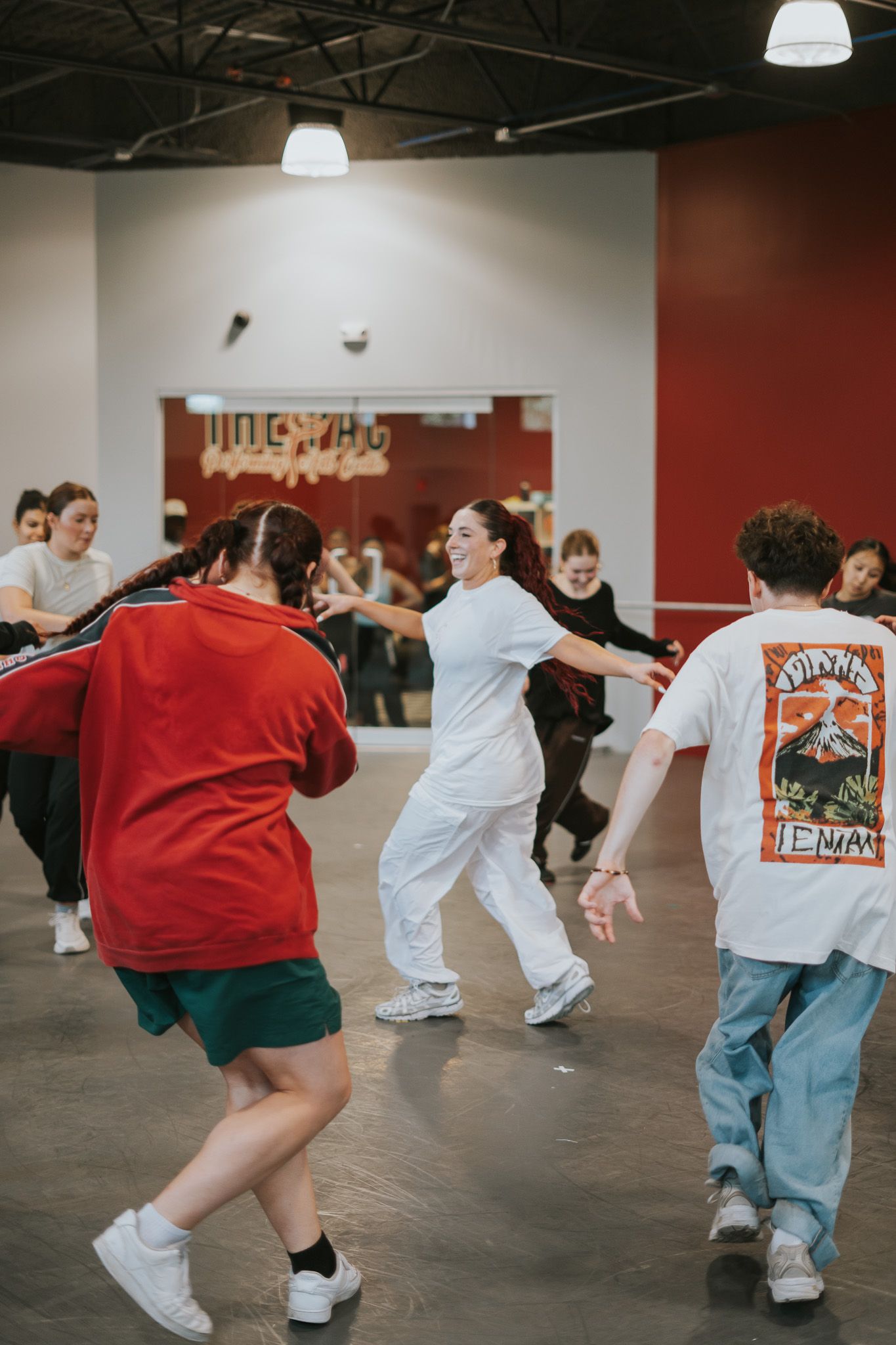 Dancers move energetically during a casual dance class in a studio with red accent walls.