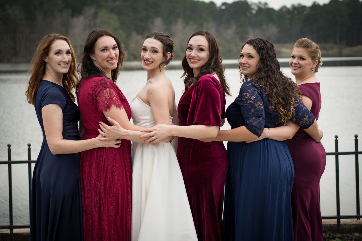 Bridesmaids in navy and burgundy dresses pose with bride in elegant wedding attire.