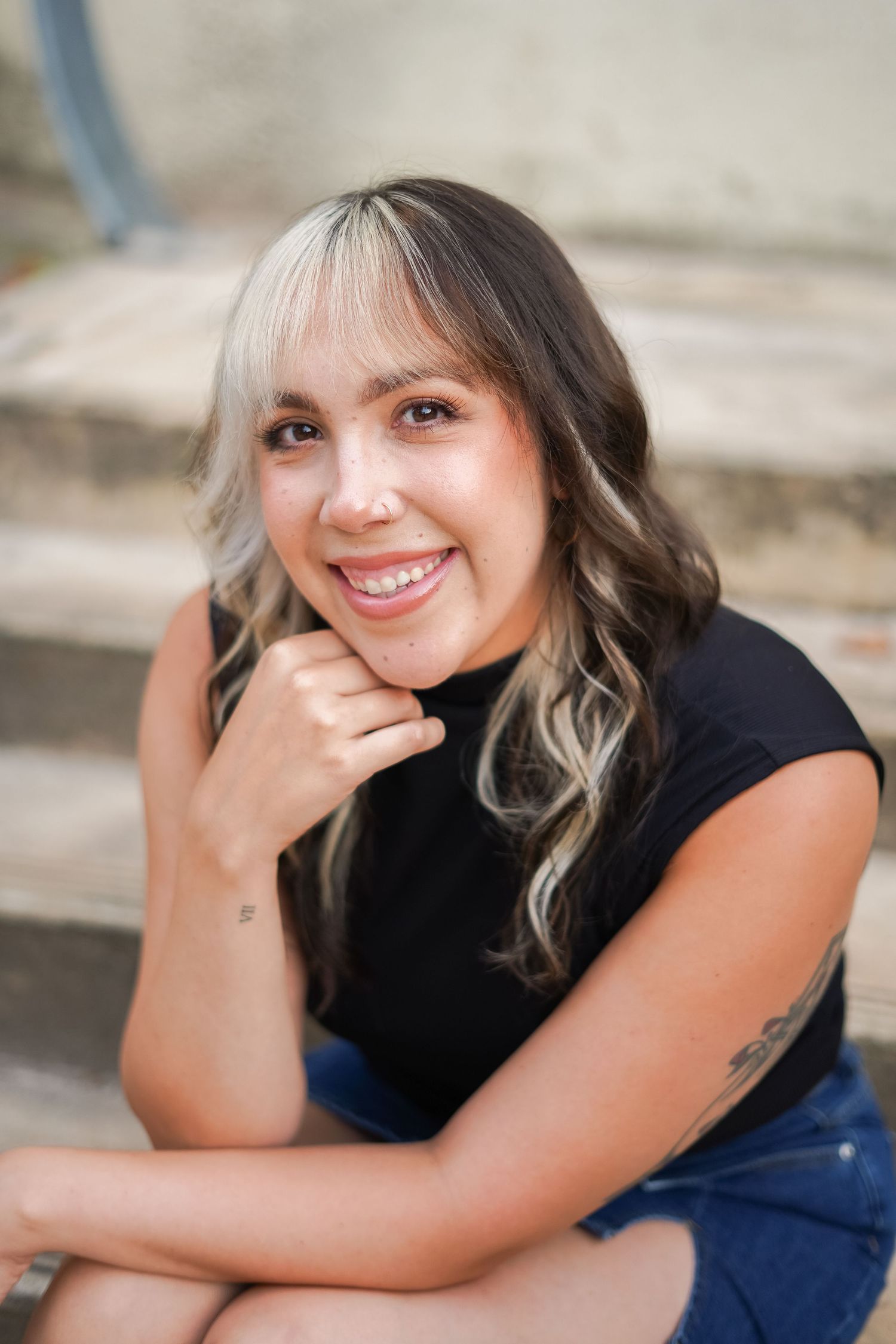Portrait of a smiling person with blonde highlights sitting on concrete steps.