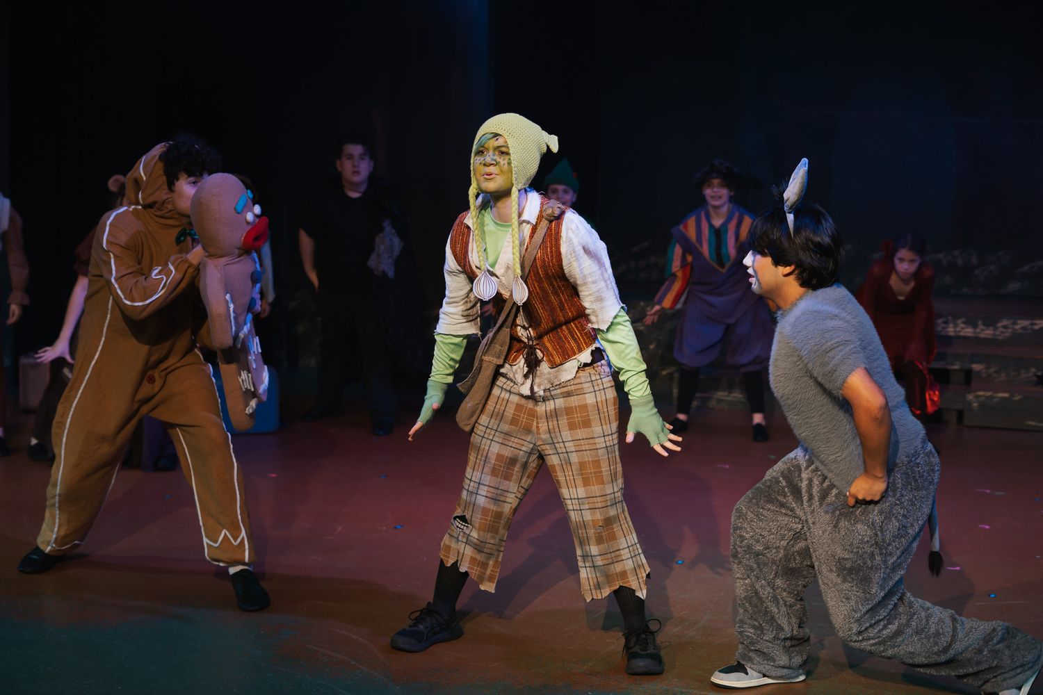 Stage production of Shrek the Musical with actors in costume performing a lively scene on a theatrical set.