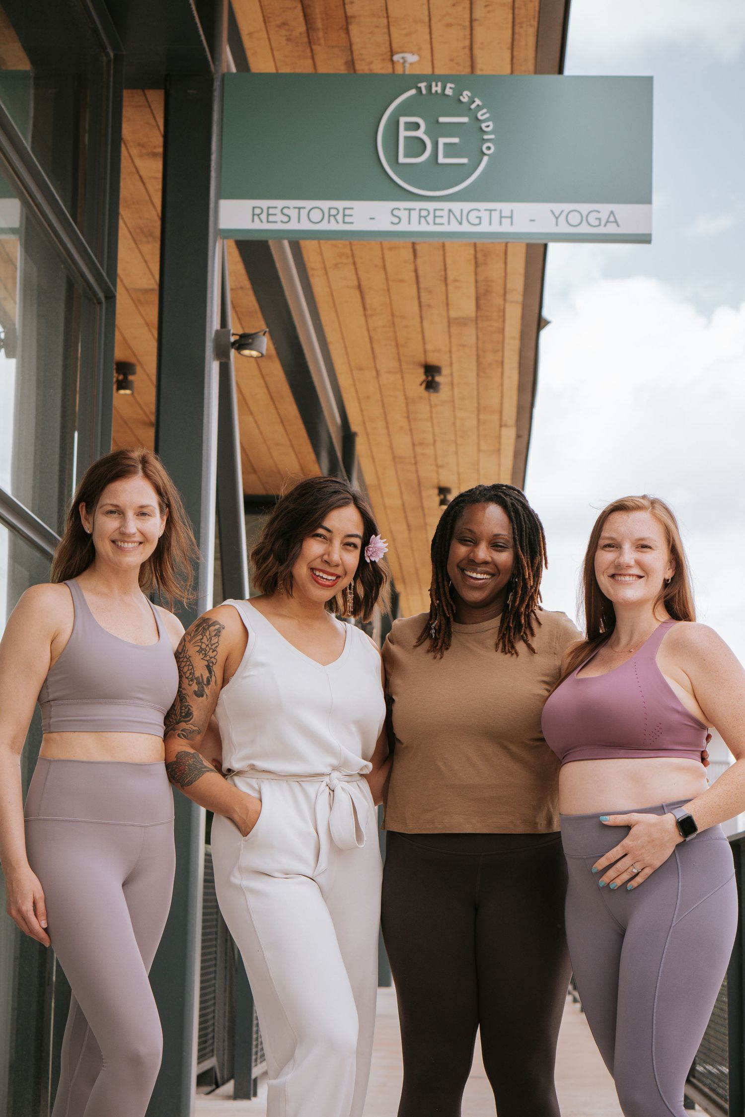 Four fitness instructors posing together outside a yoga studio in athletic wear.