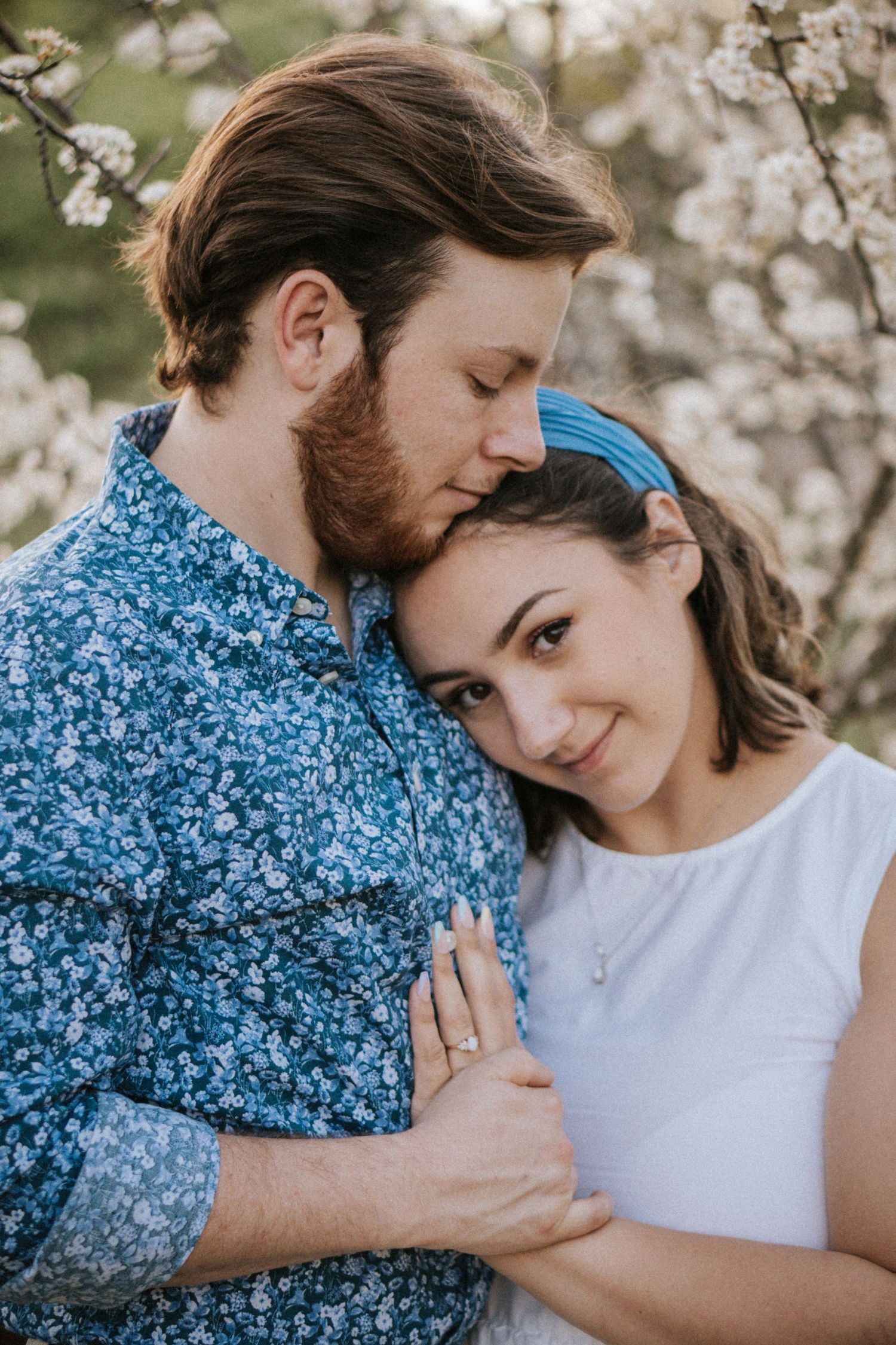 Romantic couple embracing among cherry blossoms with the woman wearing a blue headband.
