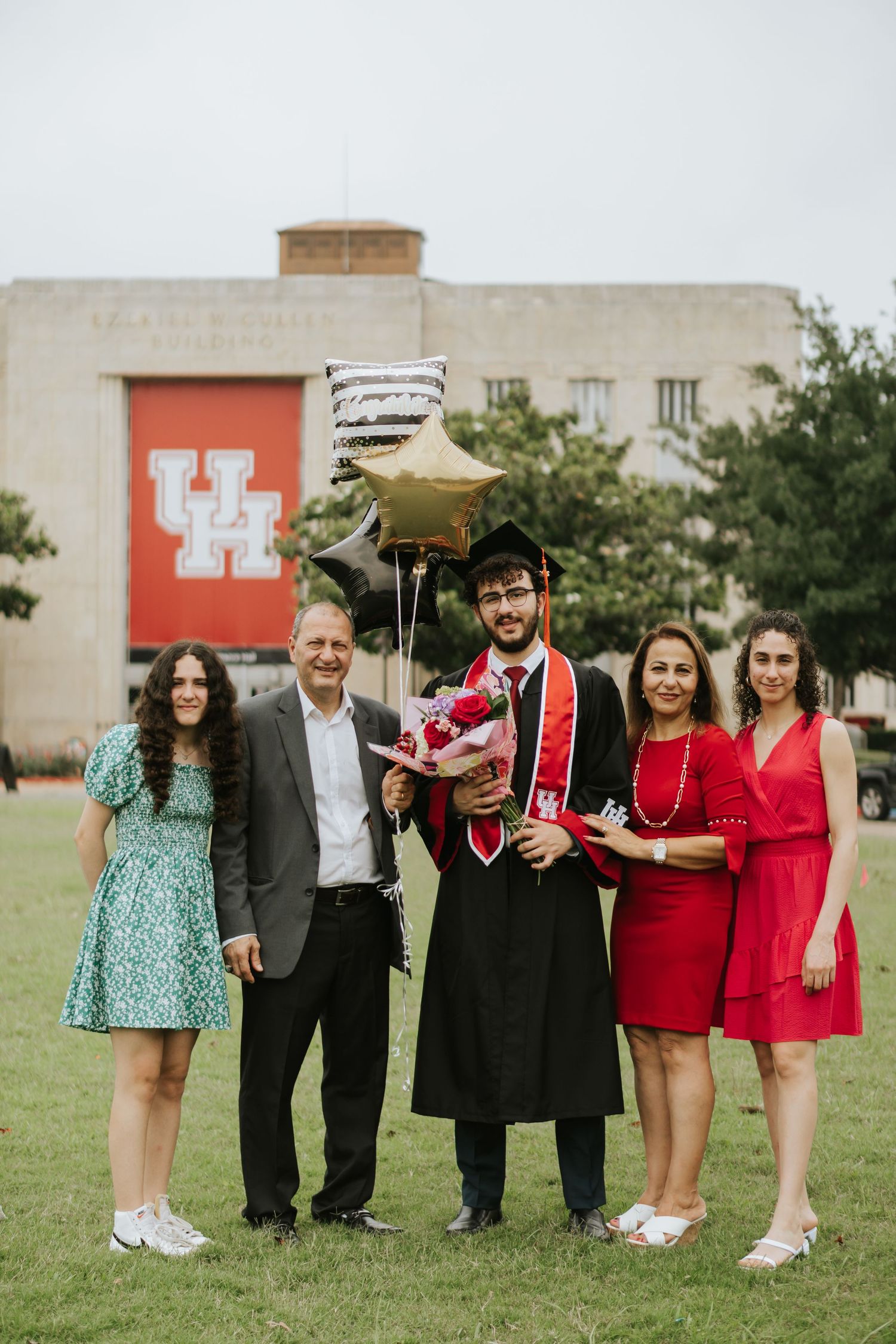 Family graduation photo at University of Houston with red logo building in background.