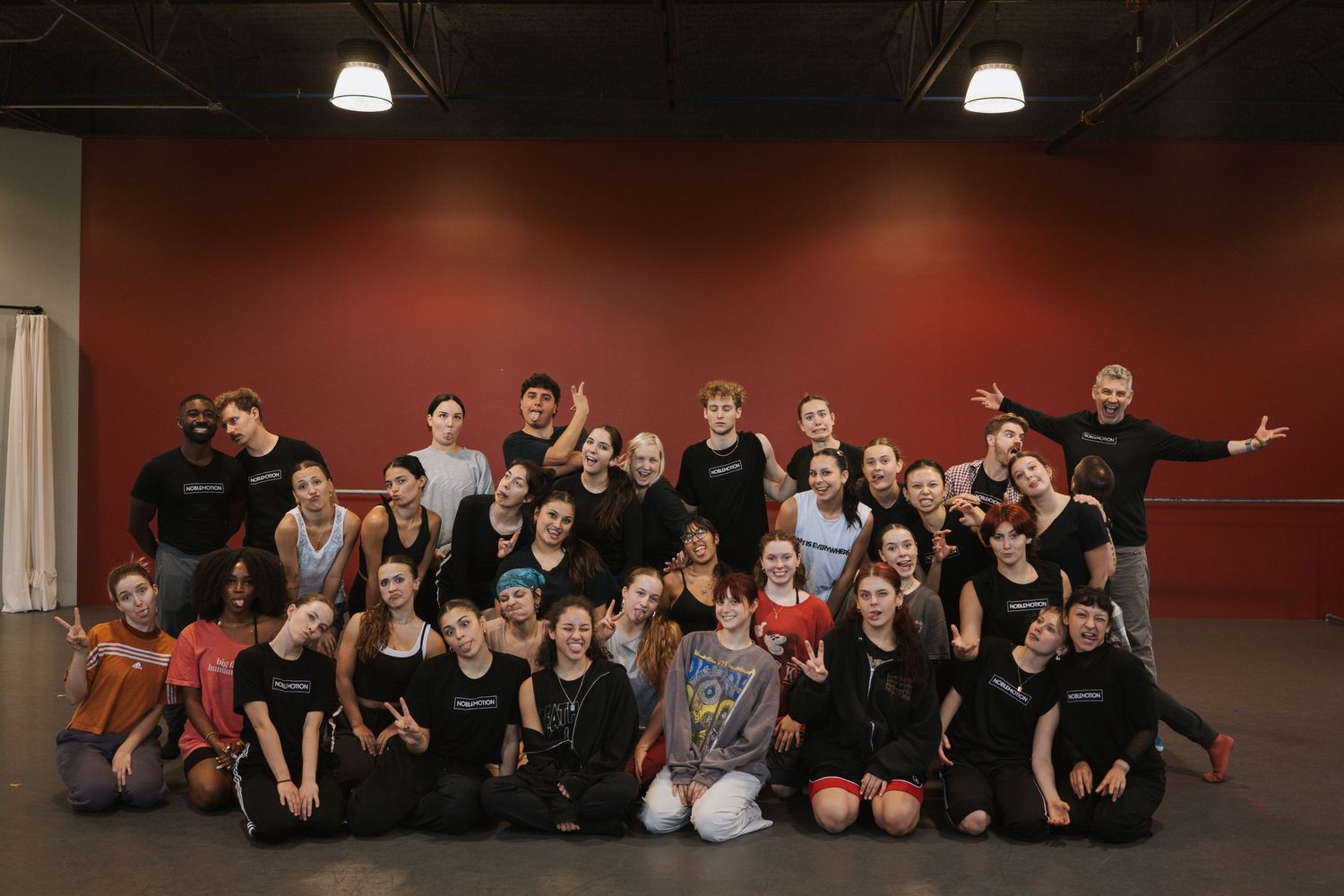 Large group of students and instructors posing together in a dance studio with red walls.