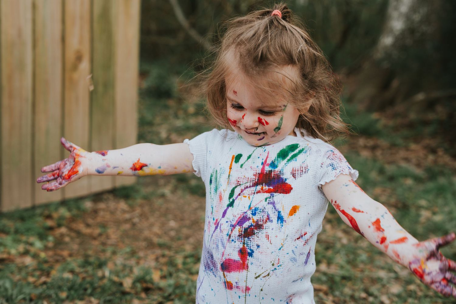 Joyful child covered in paint with arms outstretched during outdoor art session.