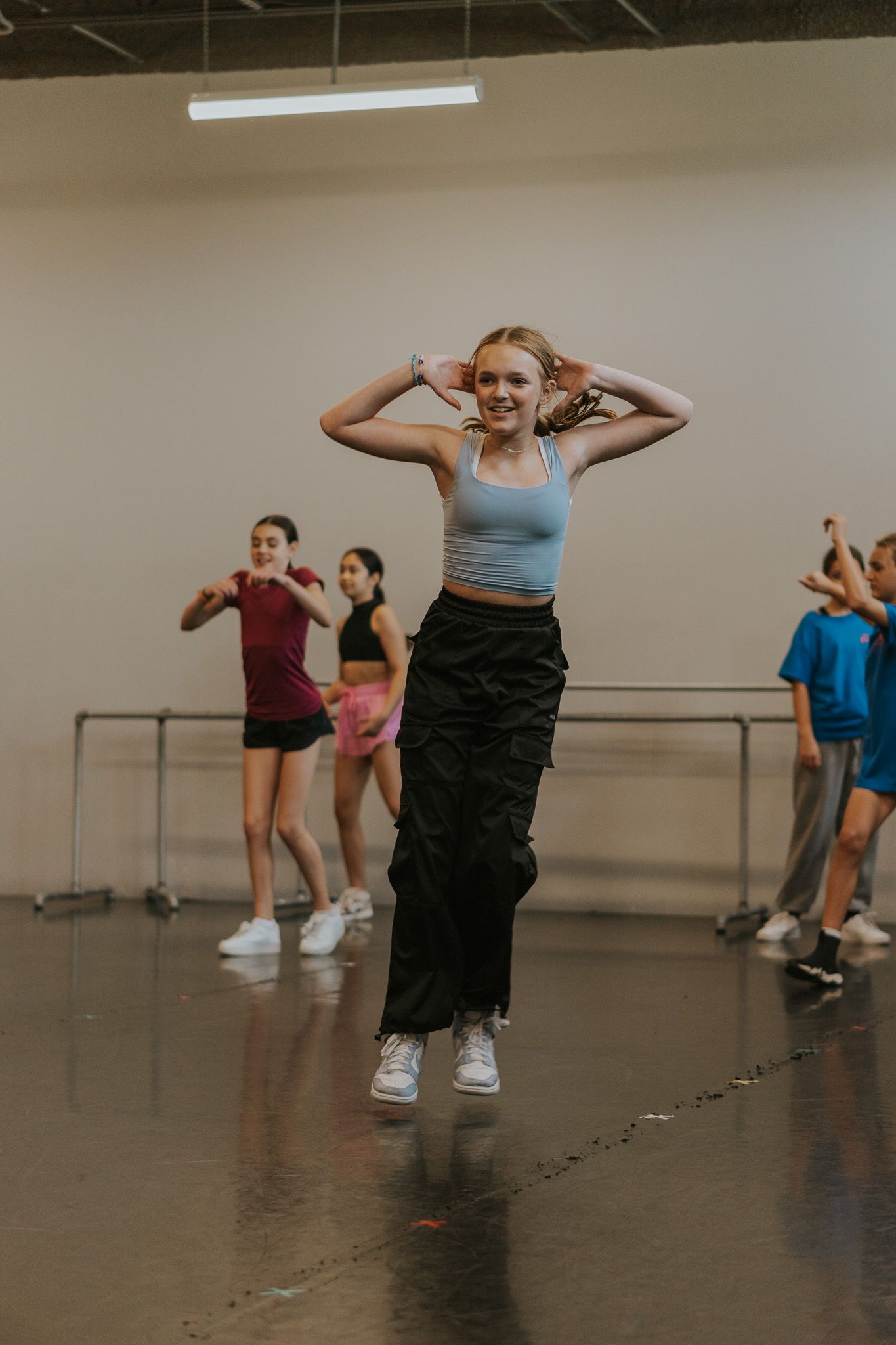 Students practicing contemporary dance moves in a professional dance studio with ballet barre.