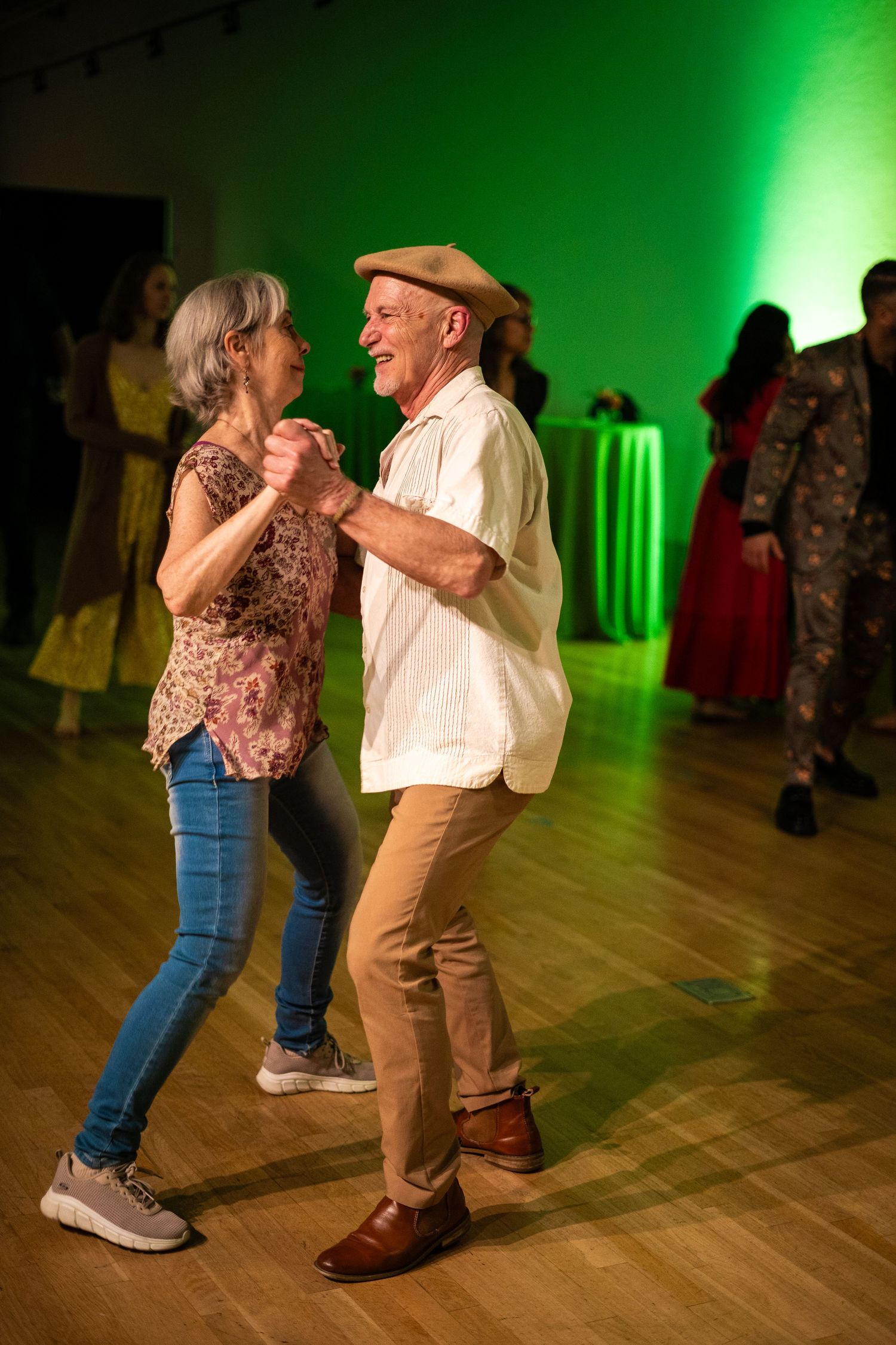 A couple dances together on a wooden floor with green ambient lighting in the background.